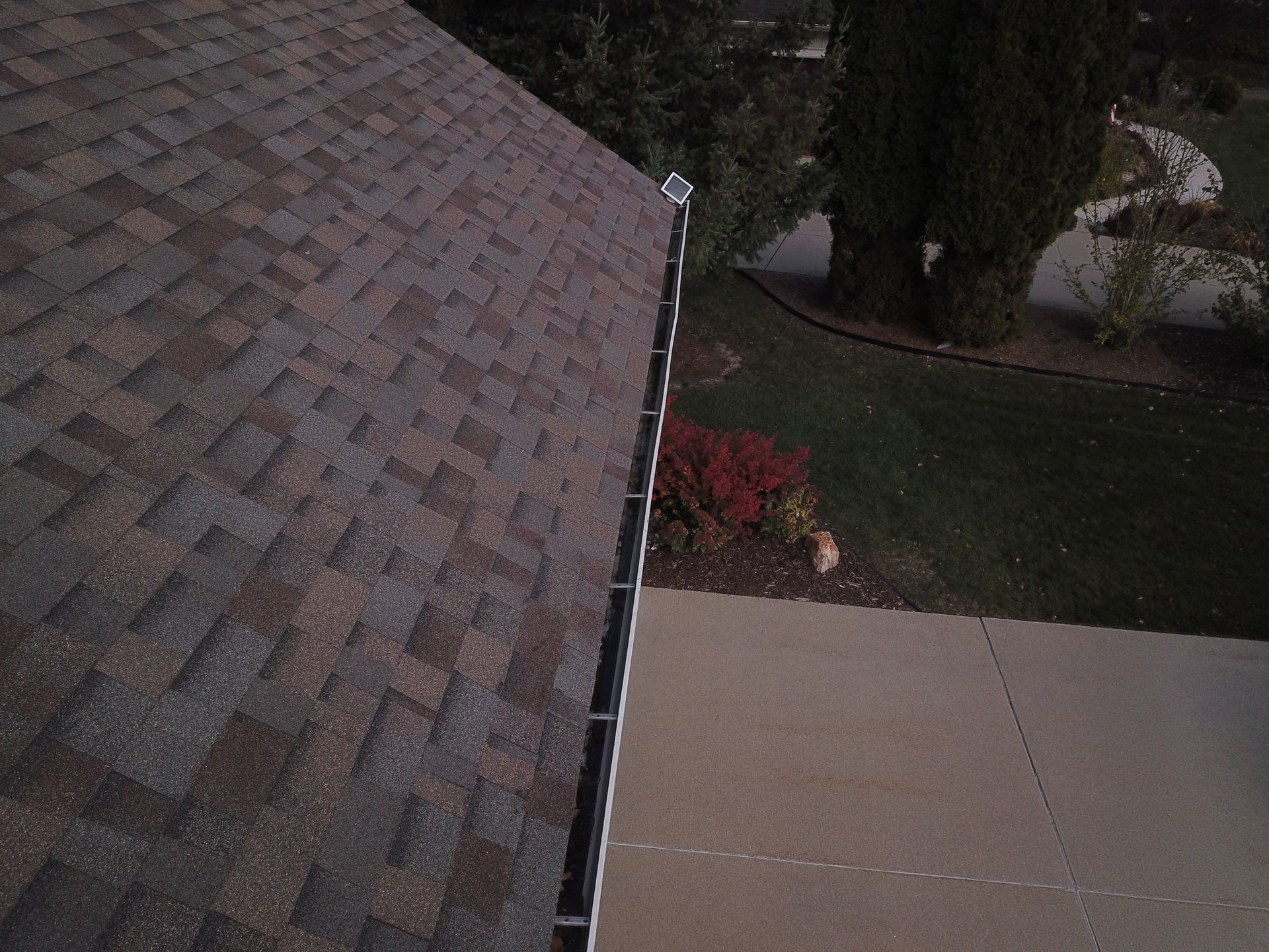 Roof shingles beside a concrete walkway and landscaped yard at dusk