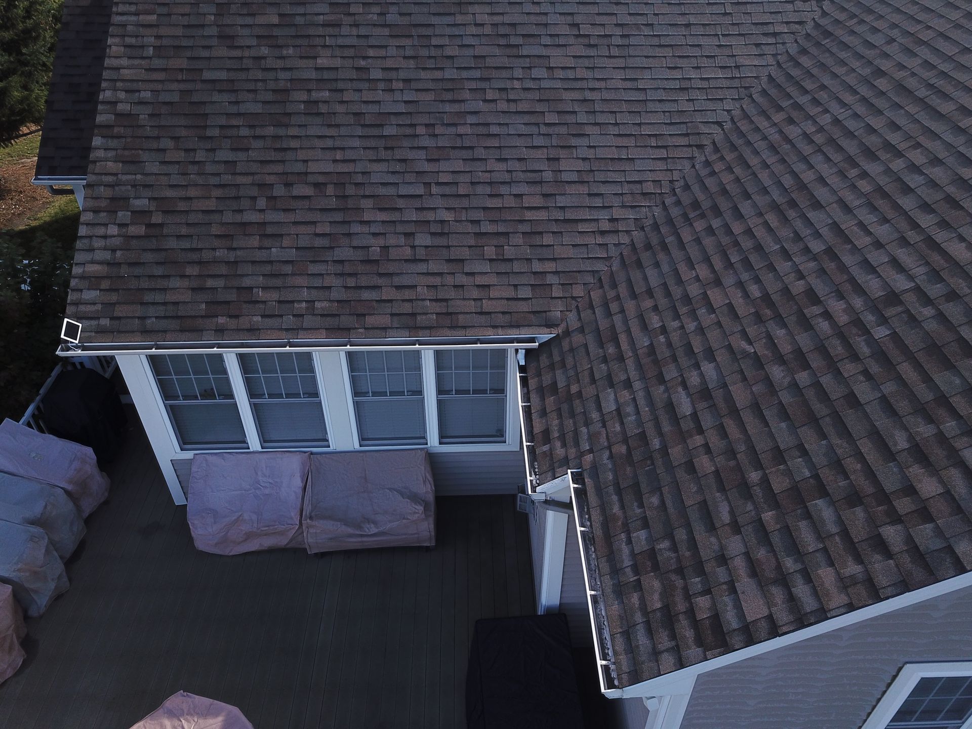 Overhead view of a house roof and patio with outdoor seating and a screened window area
