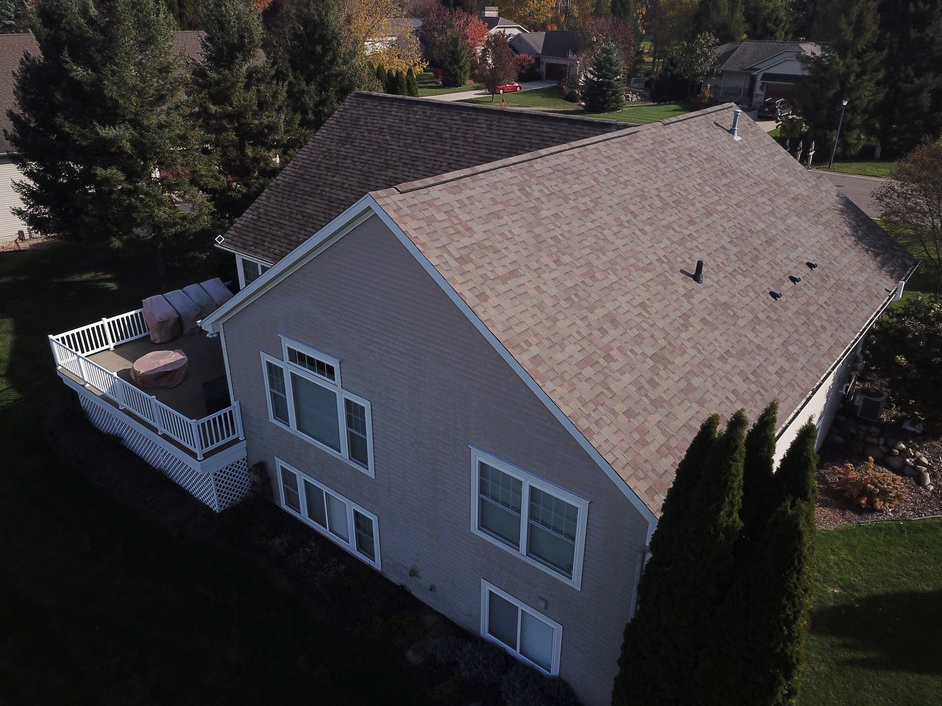 Aerial view of a beige house with a shingled roof, white deck, and trees surrounding it.