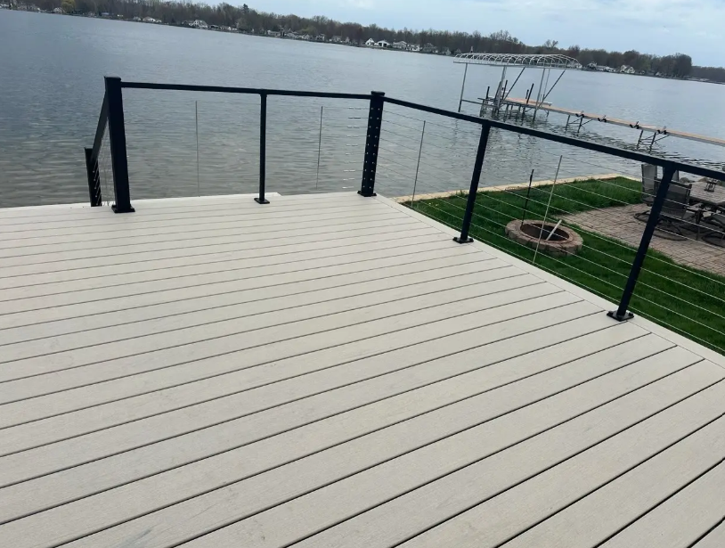 Waterfront deck with black railing, overlooking a calm body of water and a grassy shoreline