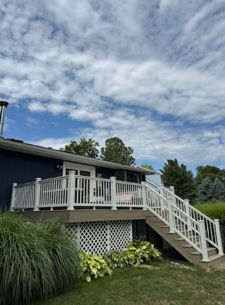 White deck stairs and railing beside a blue house, under a cloudy sky with green shrubs below