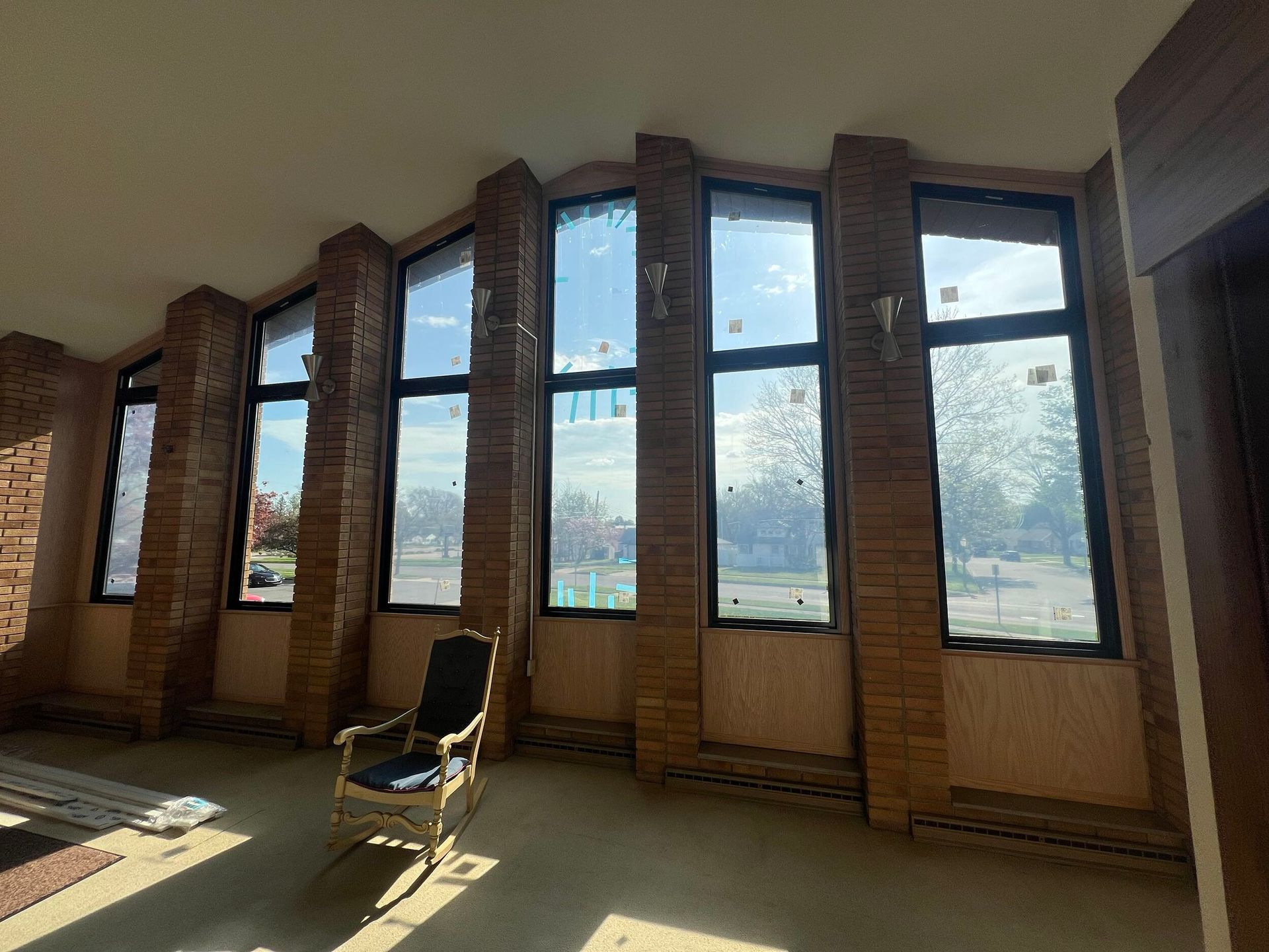 Sunlit room with tall windows, brick walls, and a single chair by the wall