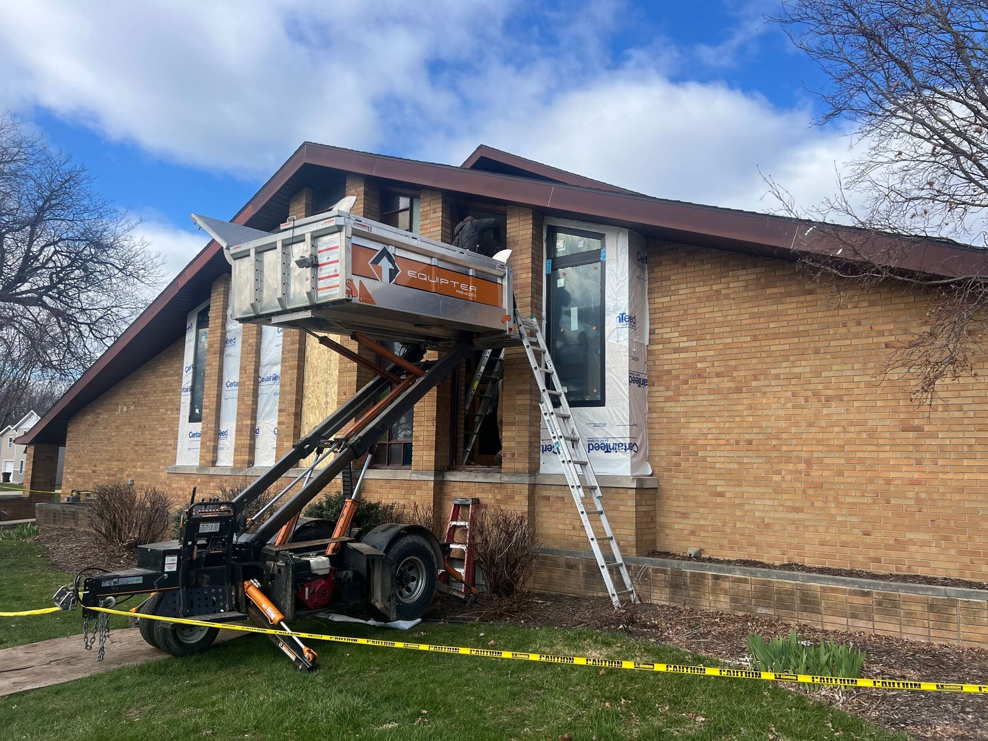 House with exterior lift and ladder beside a brick wall, under repair on a cloudy day