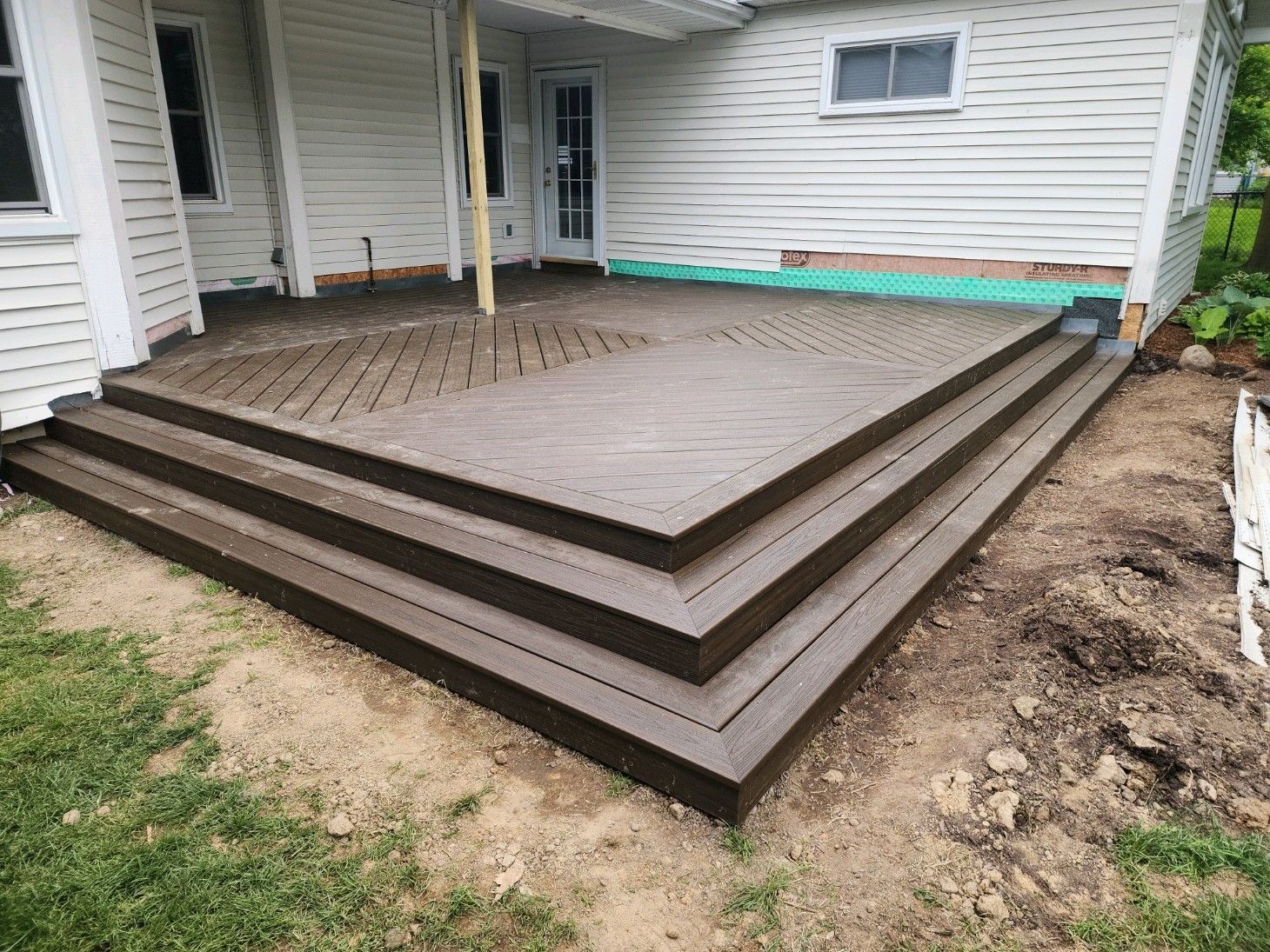 Backyard wooden deck steps leading to a white-sided house porch