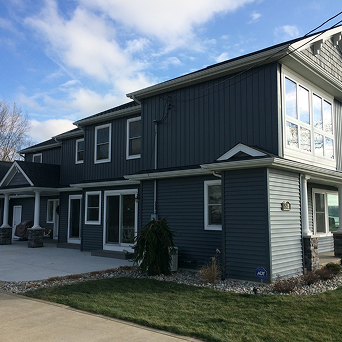 Two-story dark blue house with white trim and a small lawn under a partly cloudy sky