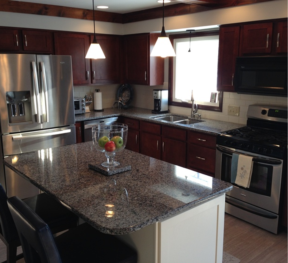 Modern kitchen with stainless steel appliances, dark cabinets, and a granite island with a fruit bowl