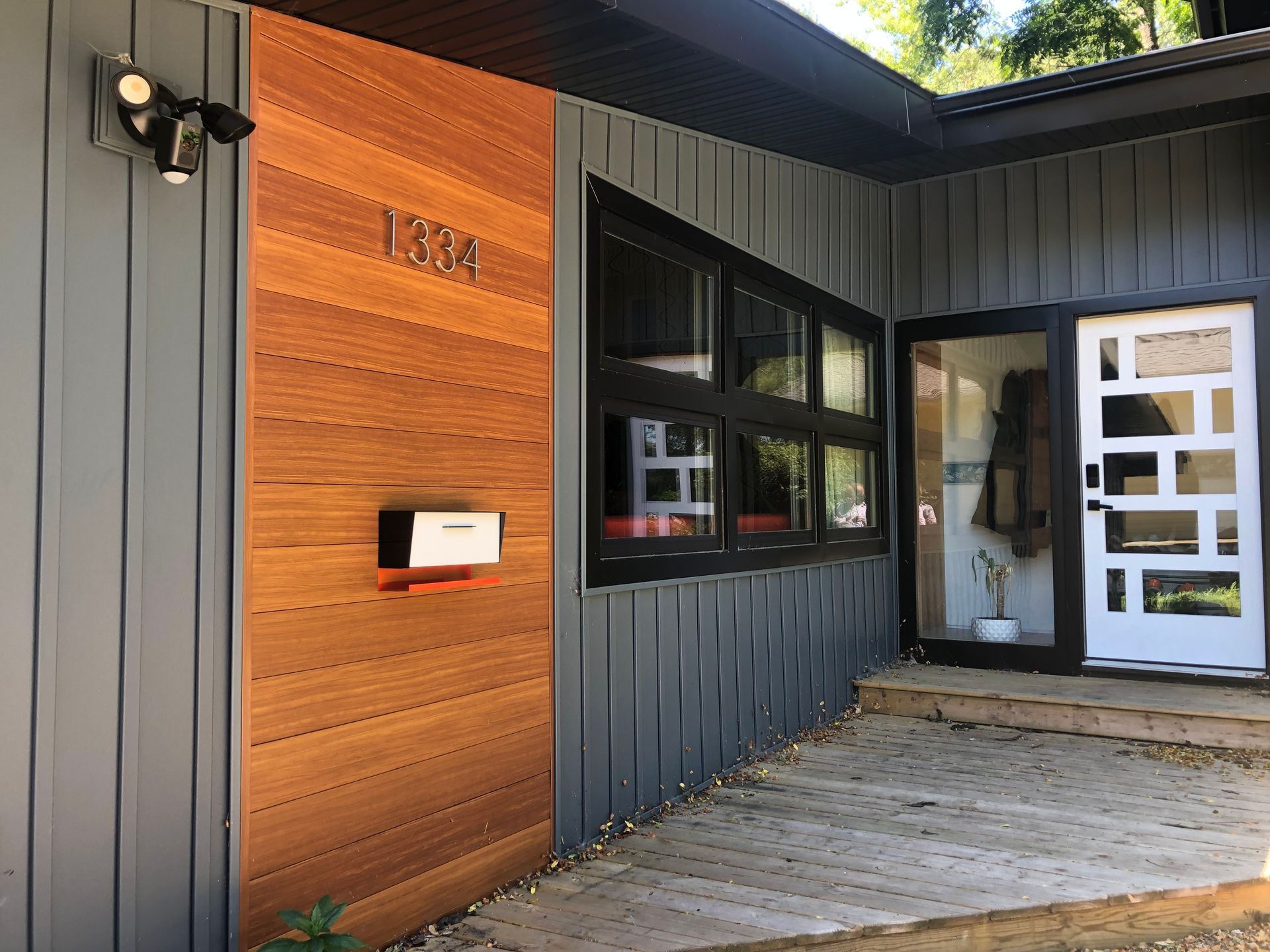 Modern house entryway with dark siding, wood accent wall, and white front door