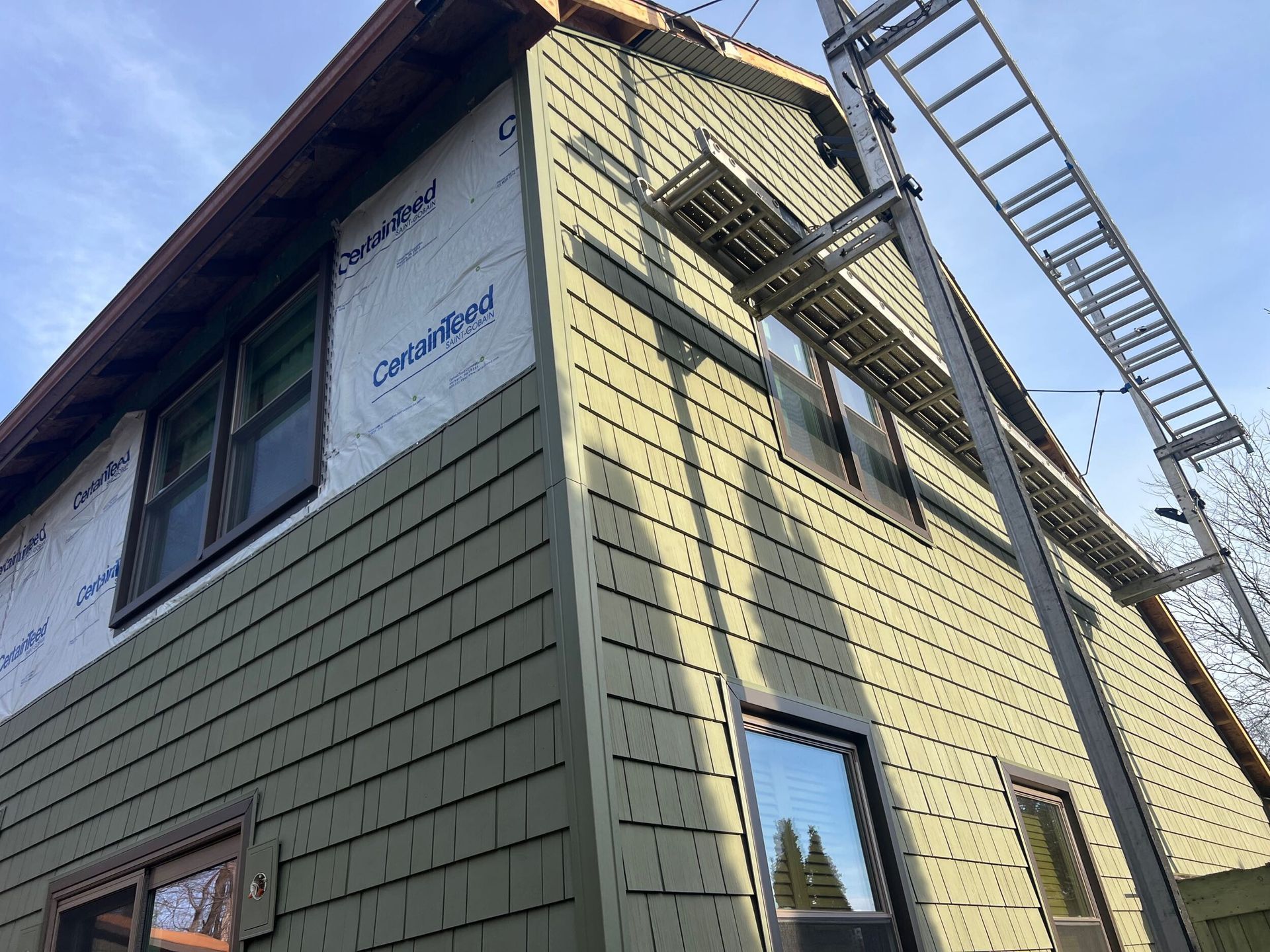 Two-story green house exterior with ladder and solar panel on the roof