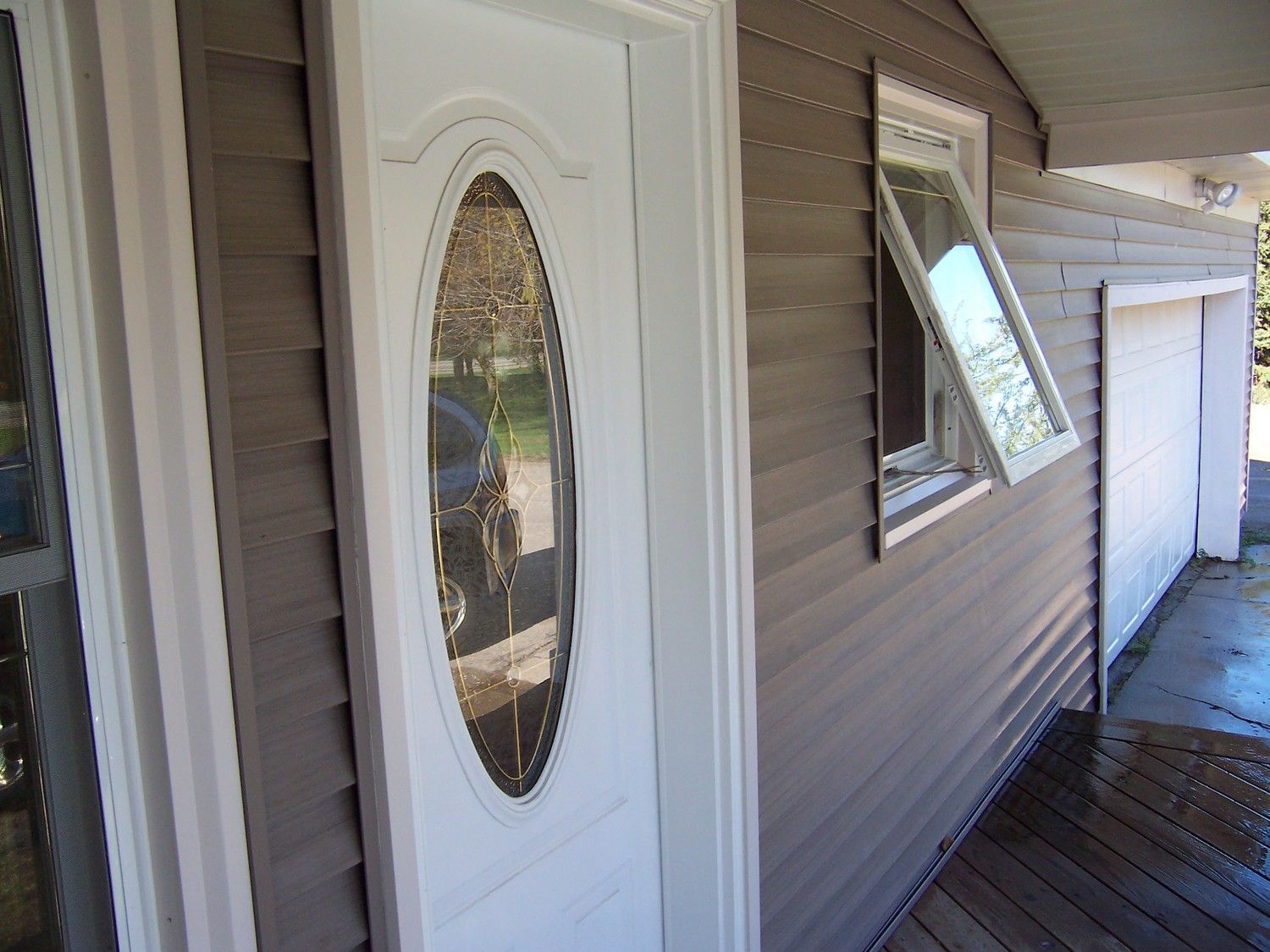 White front door and tan siding beside a partially open window on a narrow exterior walkway.
