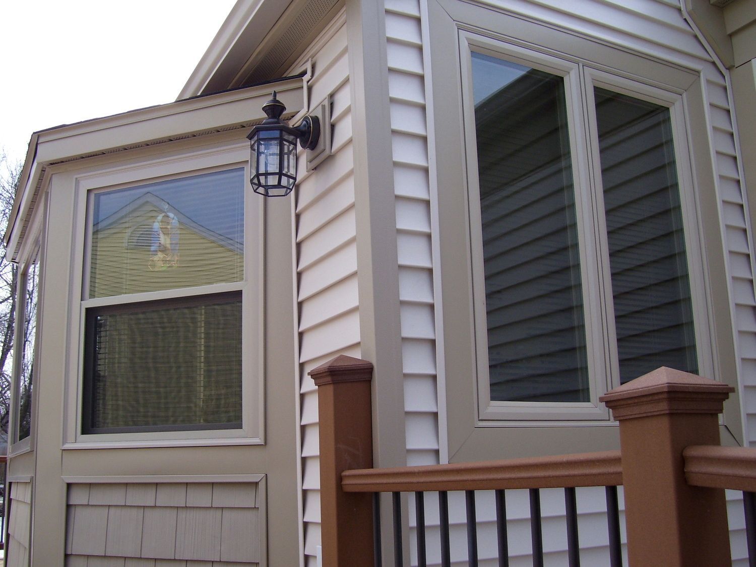 House exterior with beige siding, porch railing, large windows, and a wall-mounted lantern.