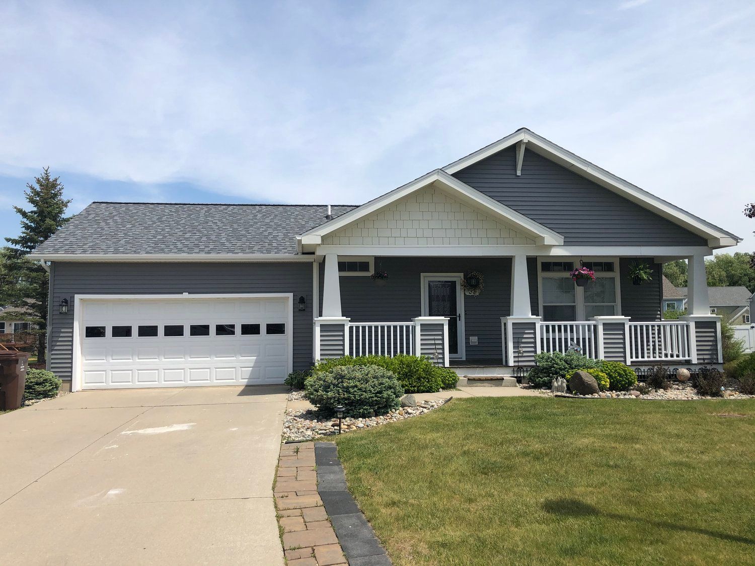 Single-story gray house with white porch, garage, and driveway on a sunny day