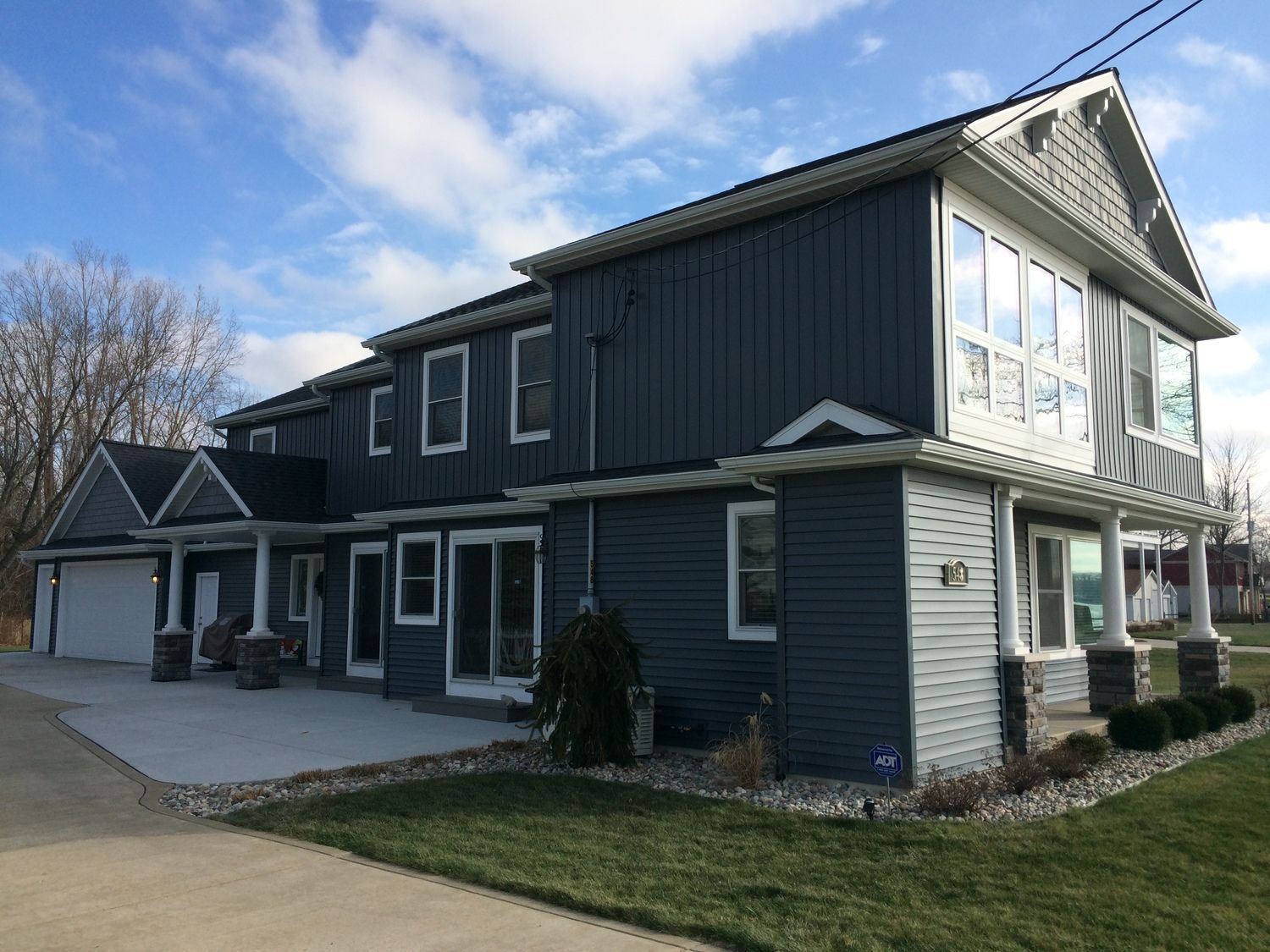 Dark gray two-story house with white trim, large windows, and a covered porch on a grassy lot.