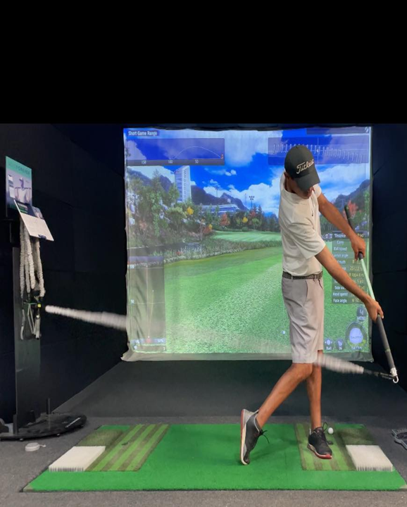 A man is swinging a golf club in front of a large screen.