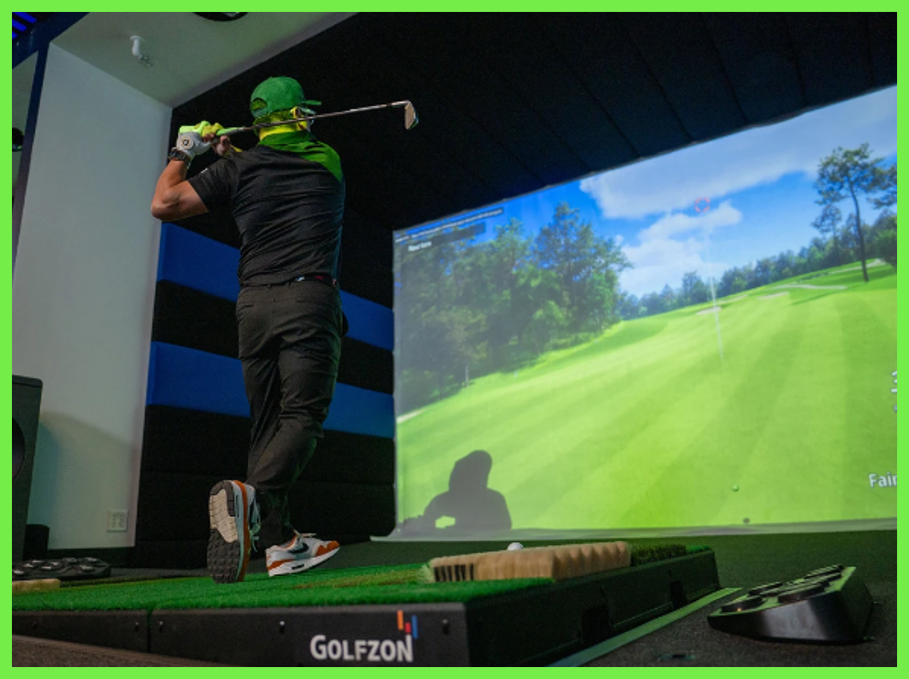 Golfer mid-swing in an indoor simulator, hitting toward a bright virtual fairway screen.