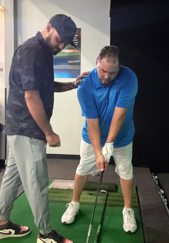 A man is swinging a golf club in front of a large screen.