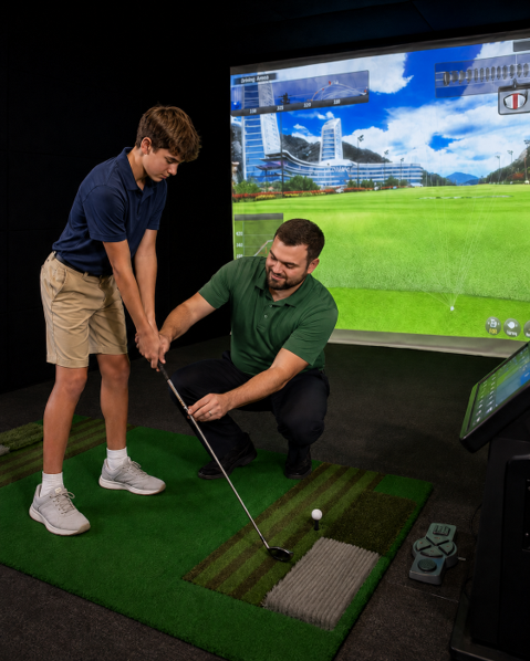 A man is swinging a golf club in front of a large screen.