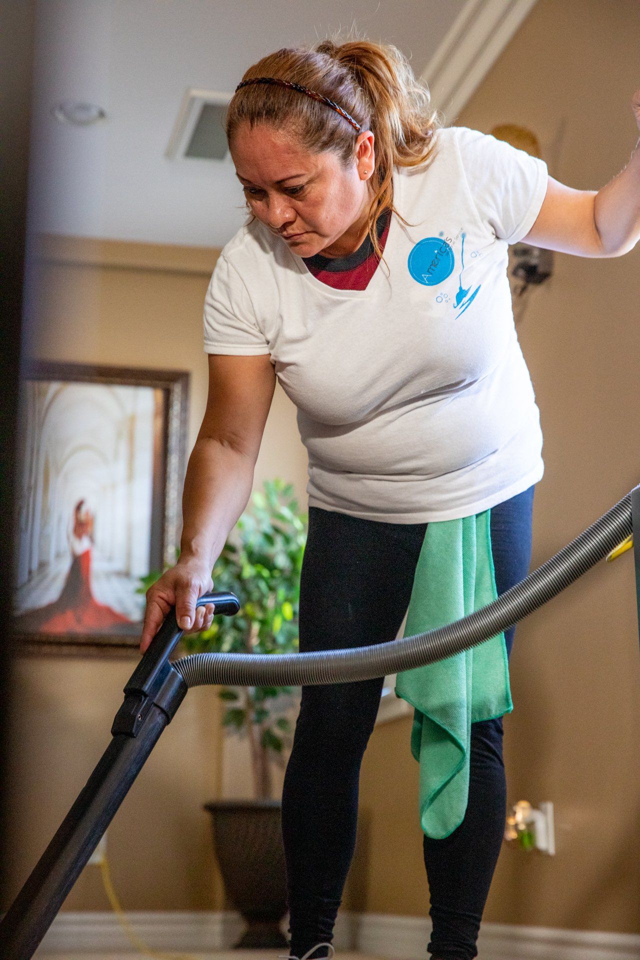Woman vacuuming a carpeted floor in a living room, using a black vacuum hose.