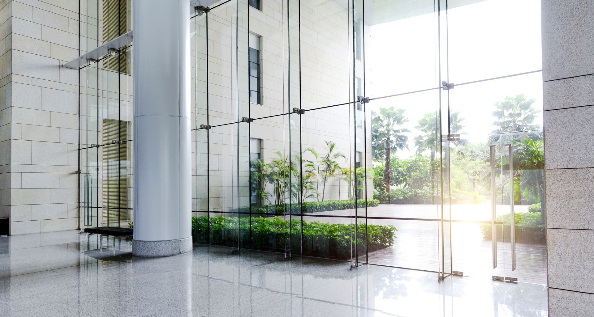 Modern glass lobby with spiral staircase, white columns, and a bright courtyard view