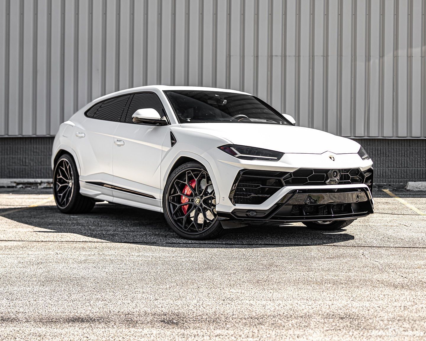 White Lamborghini Urus SUV with black accents, parked on asphalt.