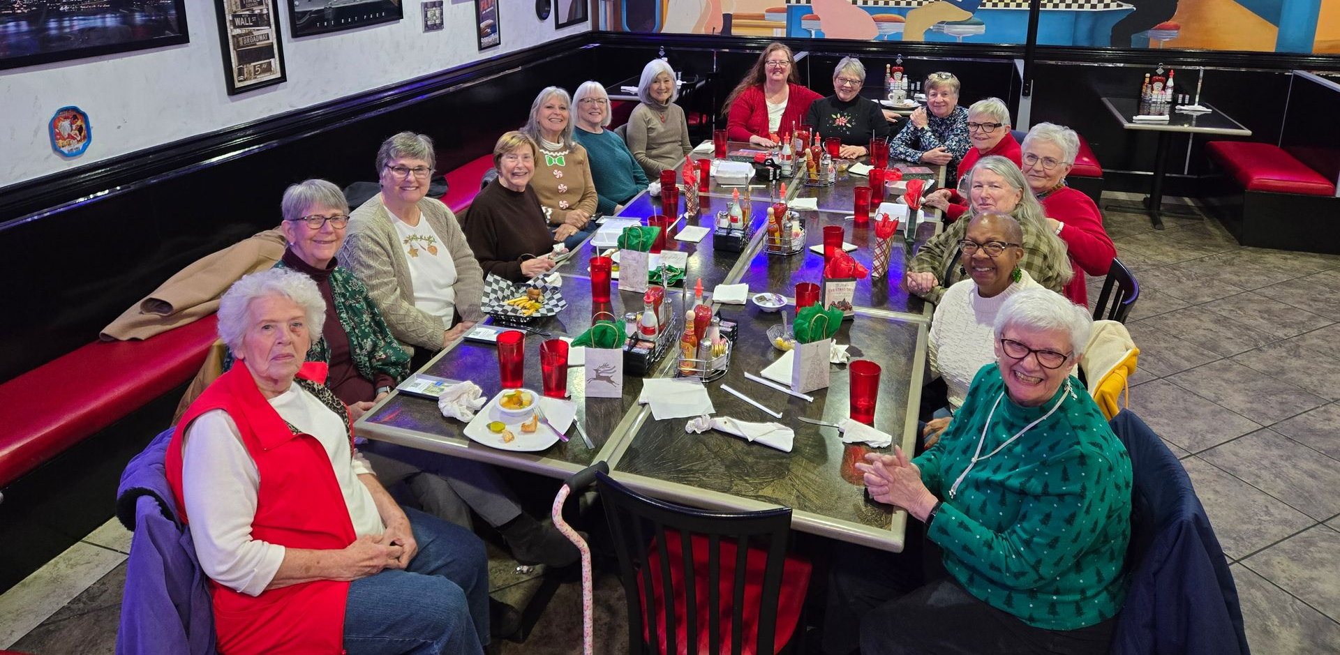 Group of people sitting at a long table in a diner. They are eating and smiling.