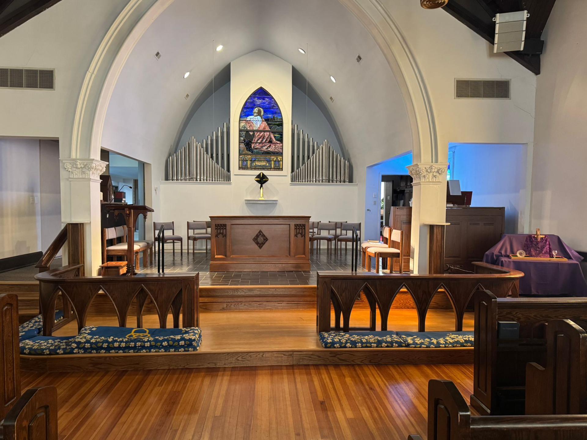 Interior view of a church sanctuary with wooden pews, altar, and stained-glass window.