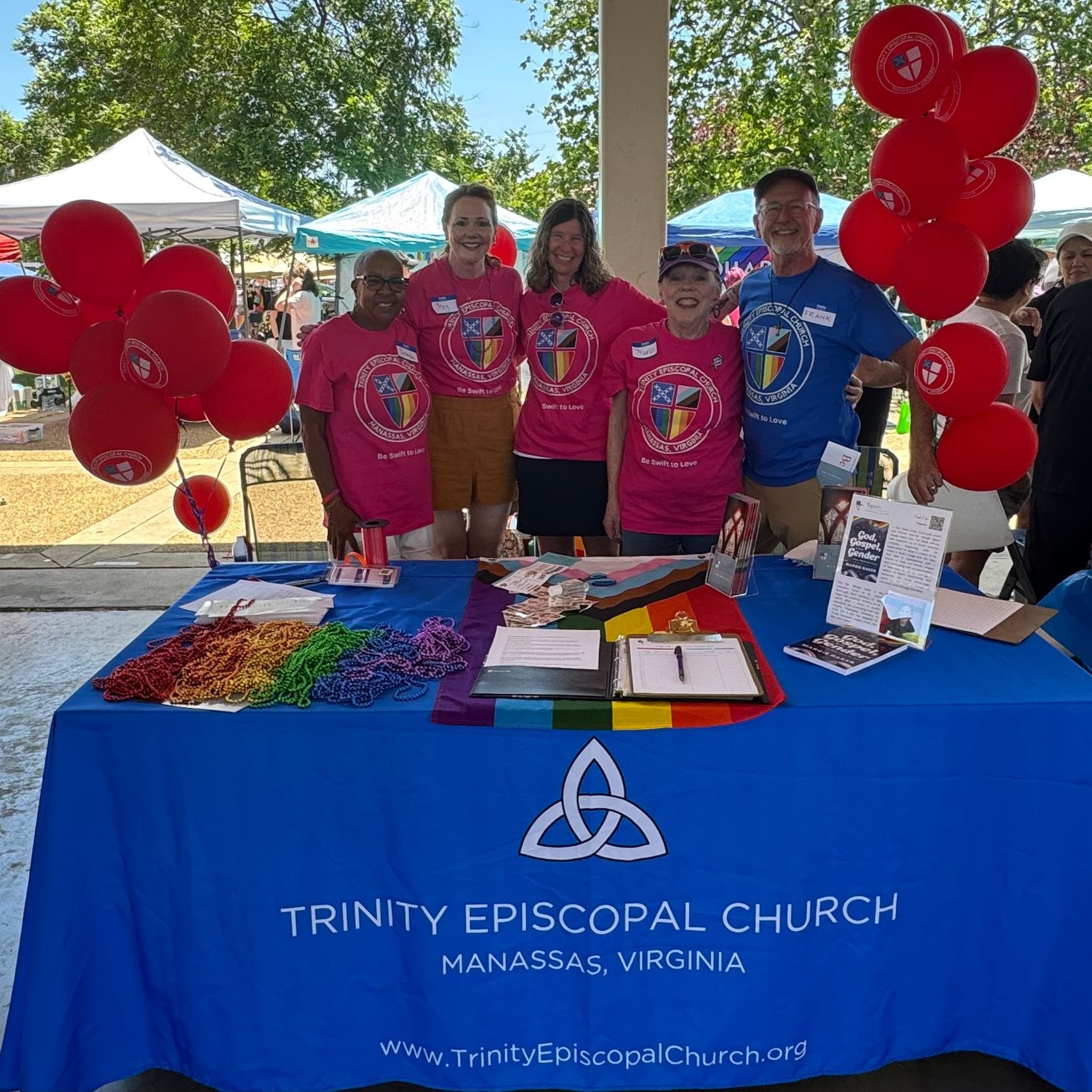 Trinity Episcopal Church booth at outdoor event with people, red balloons, and rainbow.