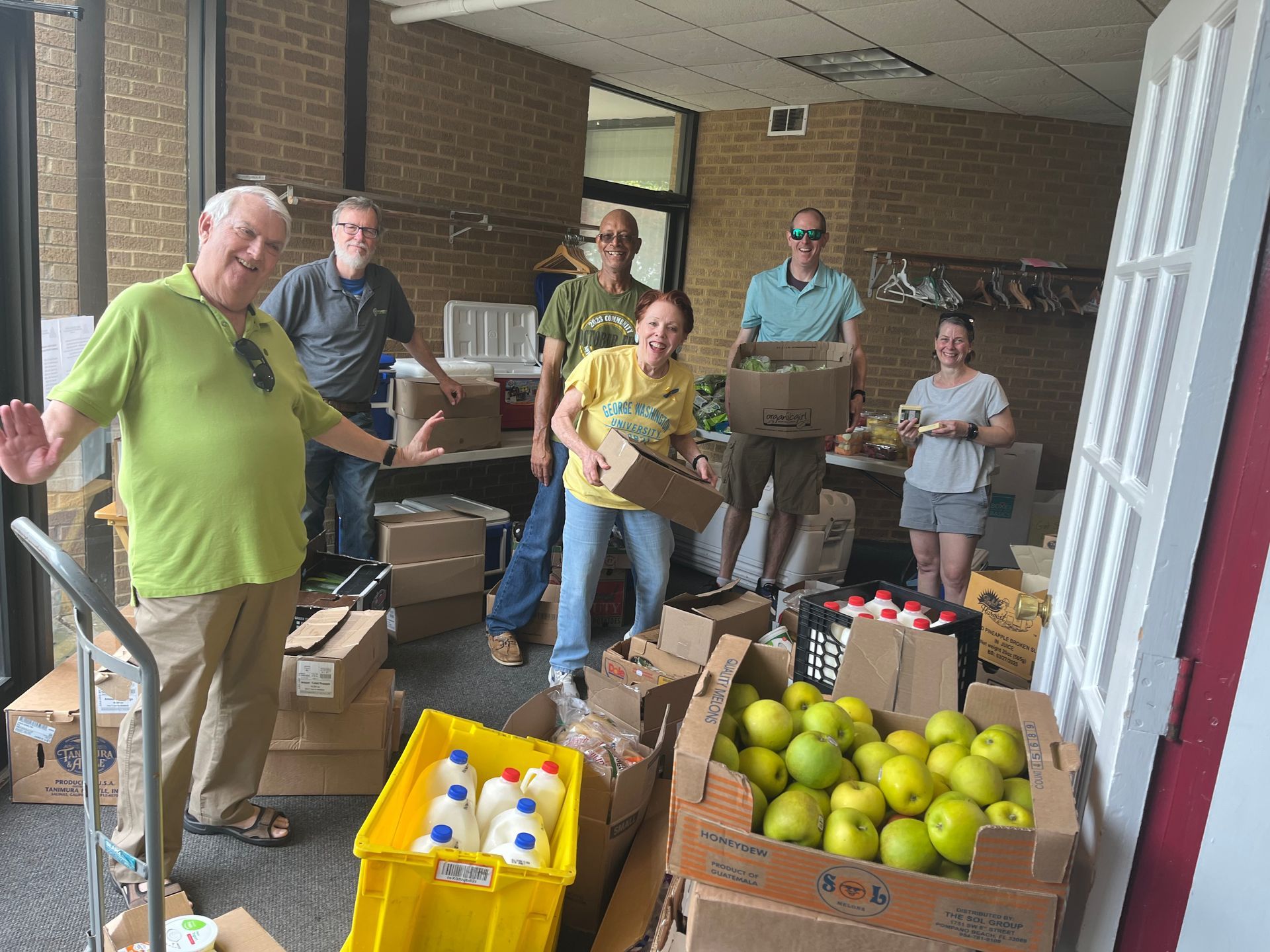 A group of people are standing in a room filled with boxes and fruit.