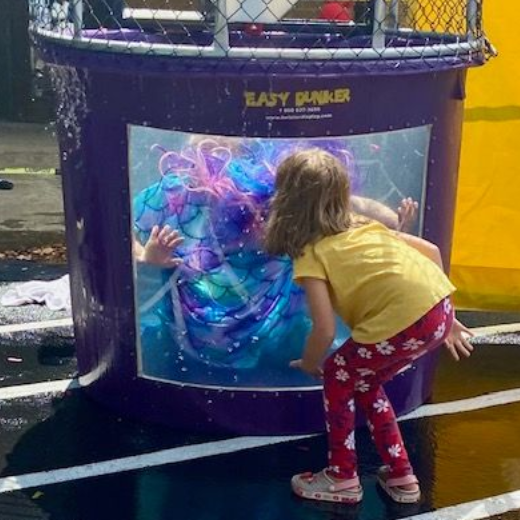 Girl looking at a person in a purple dunk tank. The person is submerged in water with colorful hair.
