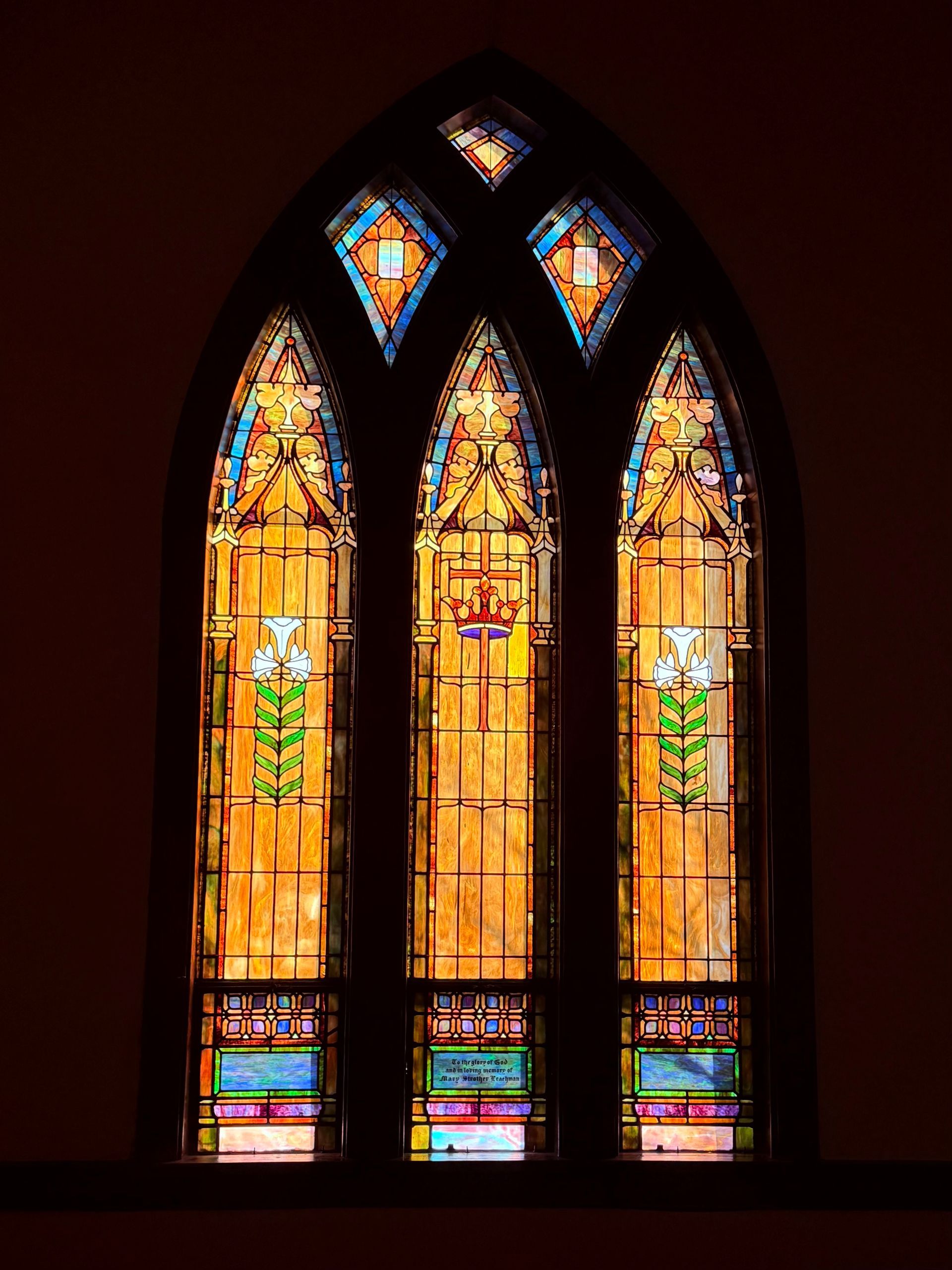 Stained glass church window, arched shape, with yellow, blue, and orange hues.