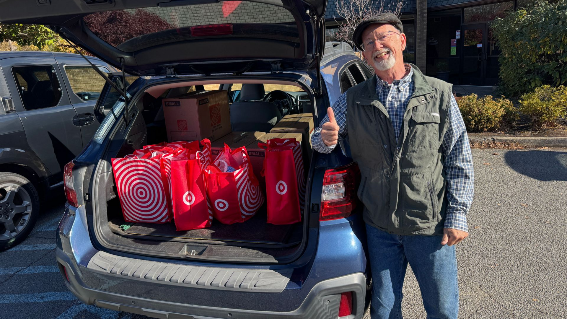 Man by car trunk full of Target bags, giving a thumbs-up. Blue car in outdoor setting.