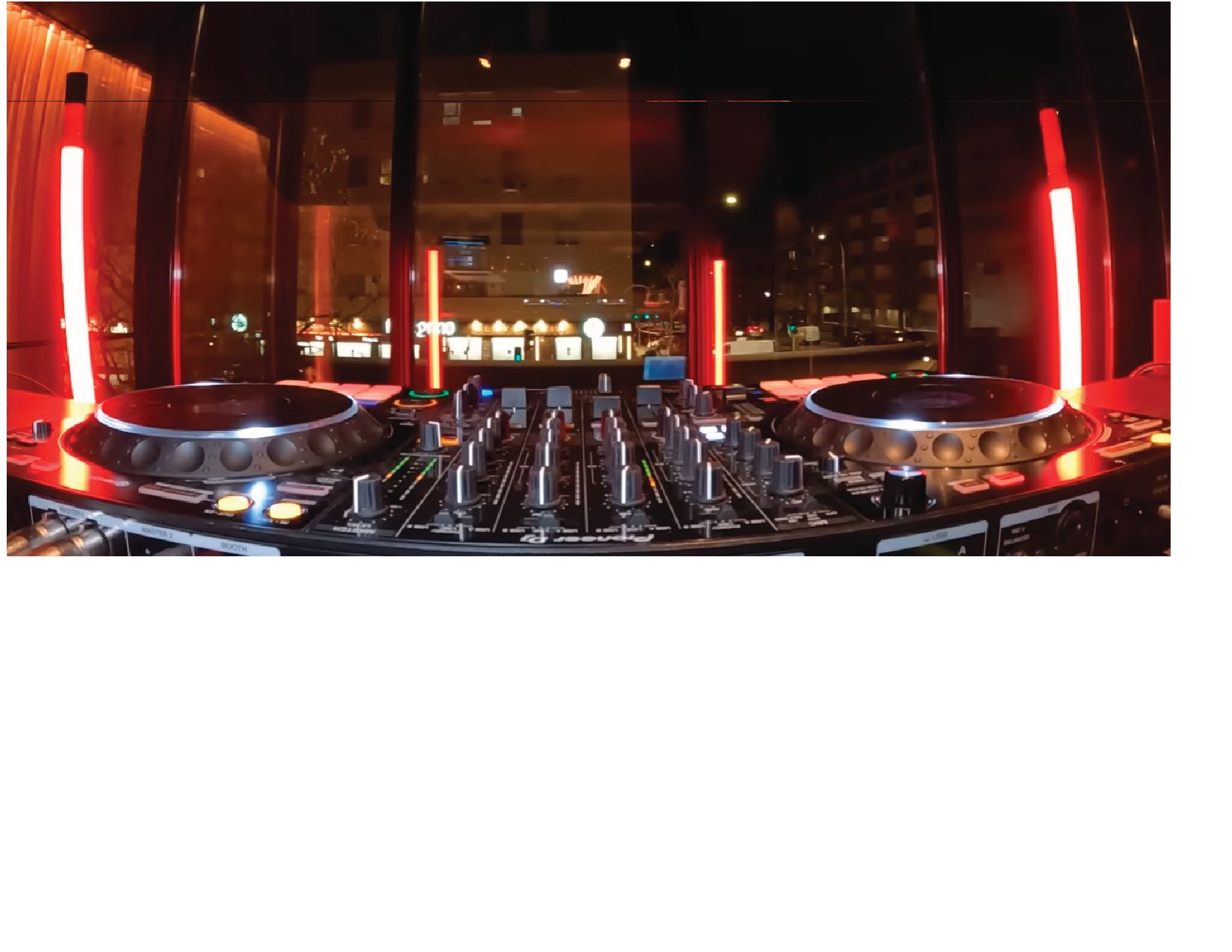 DJ booth with turntables and mixer, lit by red neon in a dim nightclub