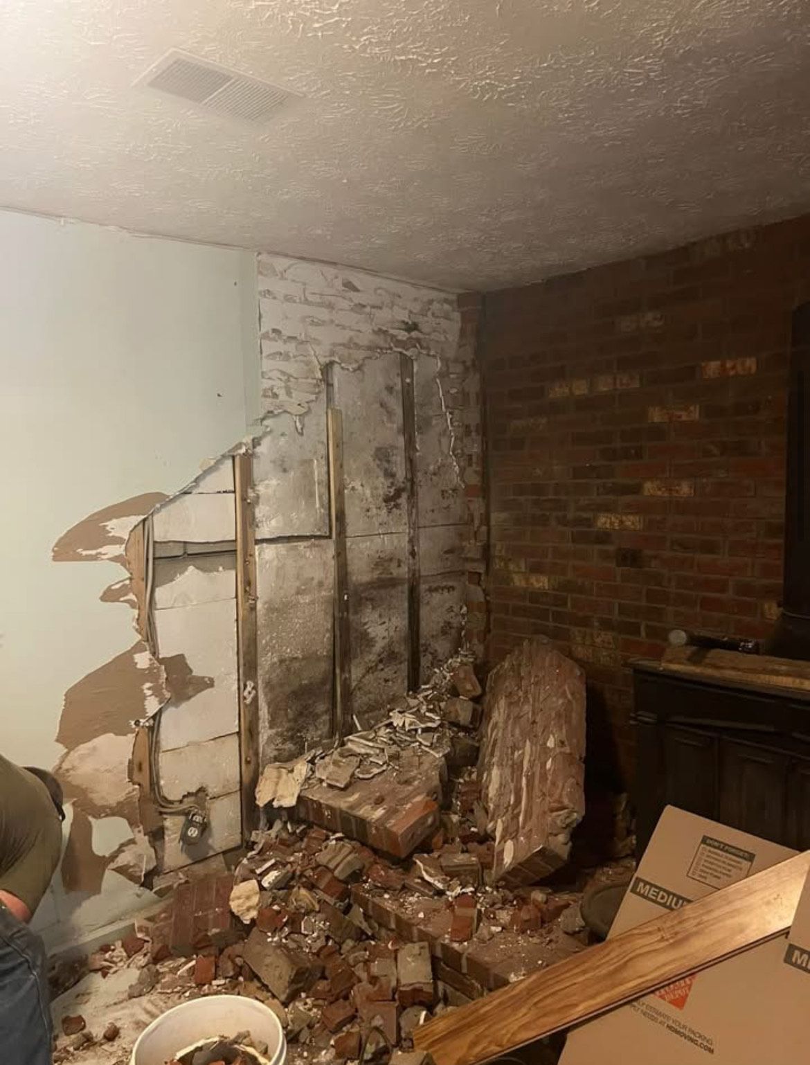 Room interior with partially demolished brick and drywall. Debris on floor, wood beams exposed.