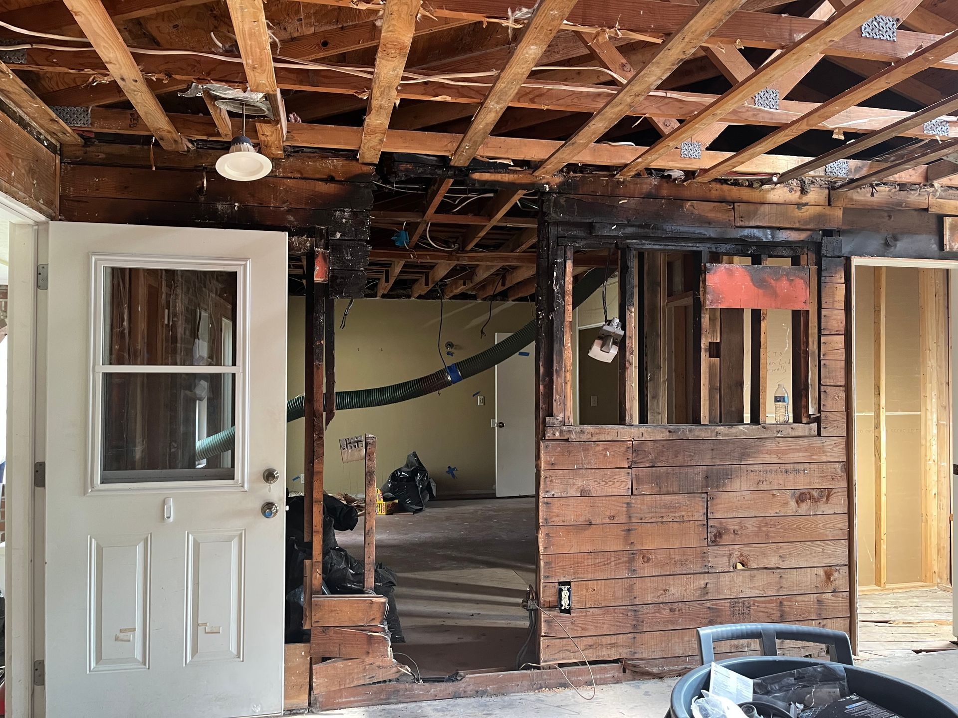 Partially demolished room with exposed ceiling joists, damaged walls, and an open door on the left