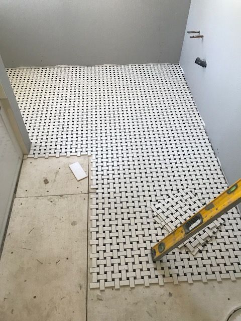 Partially tiled bathroom floor with white mosaic tiles, a yellow level, and a small unfinished section at left