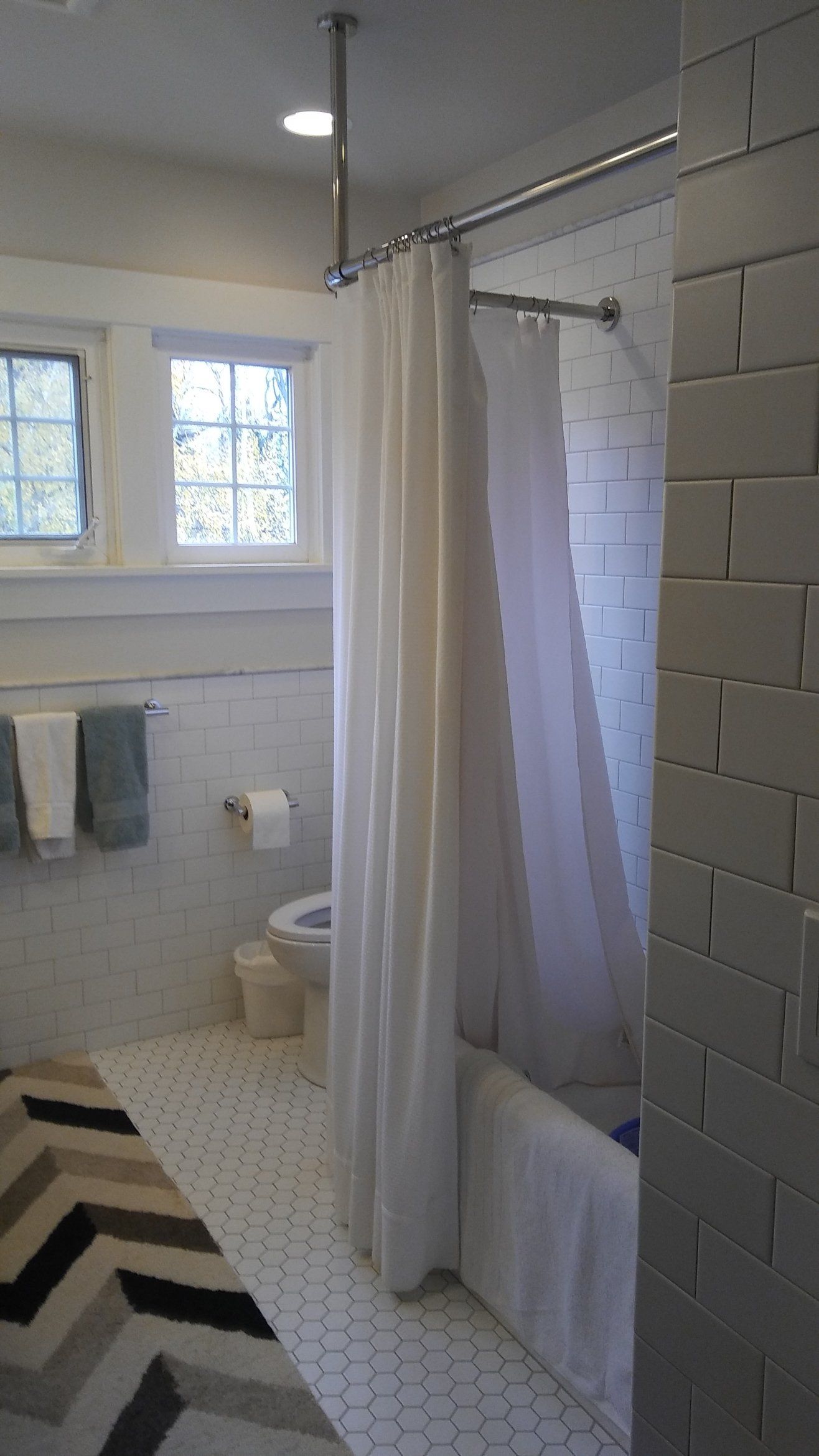 Small bathroom with a shower curtain, white tile floor, toilet, and two frosted windows.