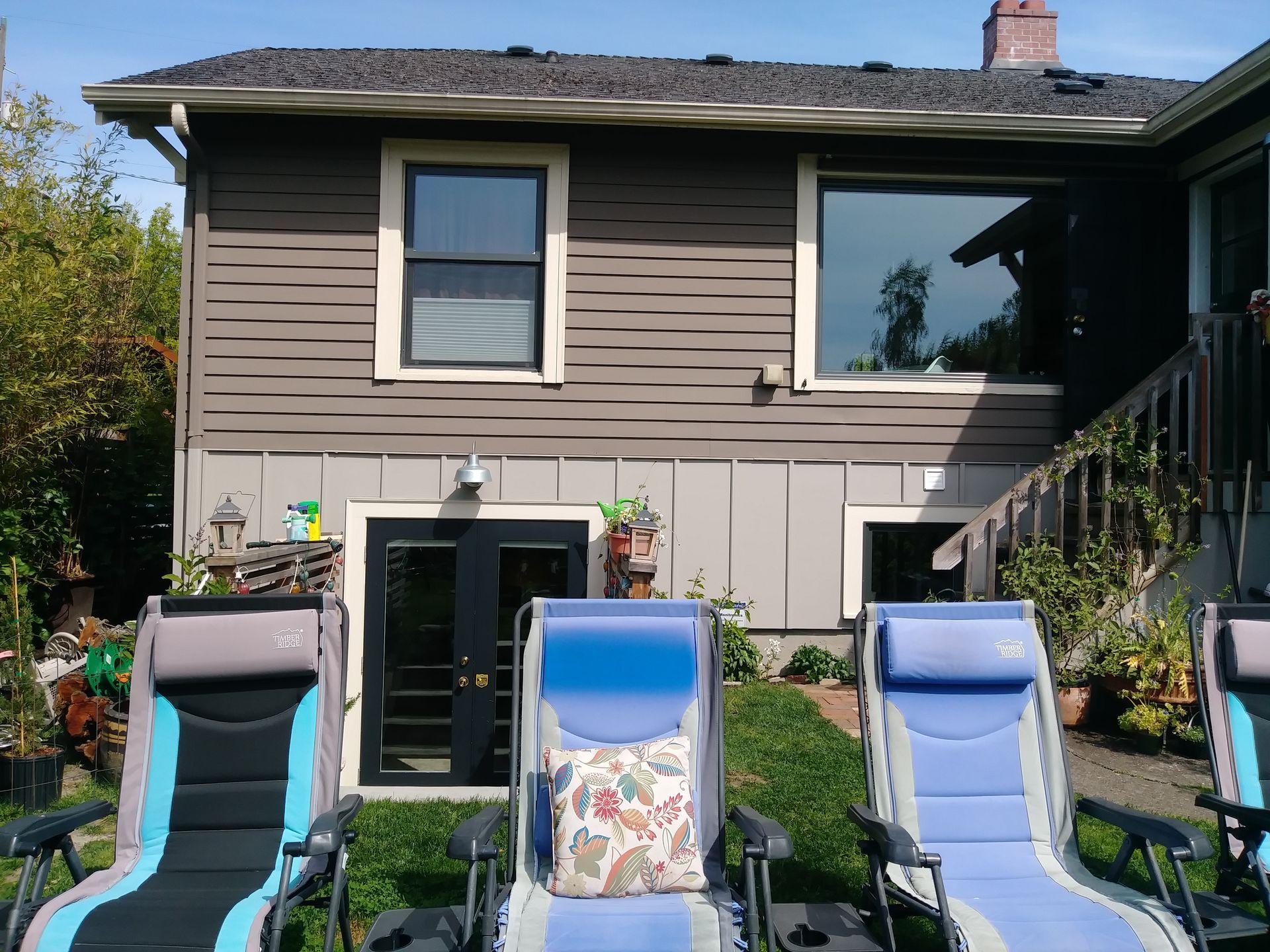 Backyard with three lounge chairs in front of a house and garden shrubs