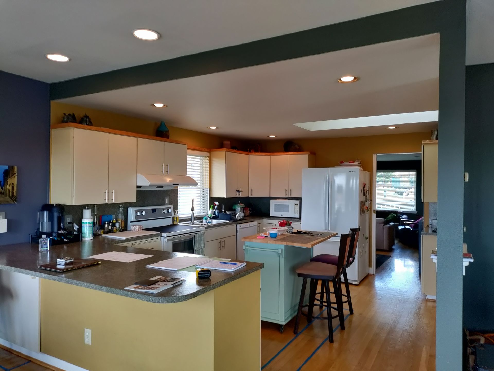 Modern kitchen with island, white cabinets, stainless fridge, and hardwood floor under recessed lighting