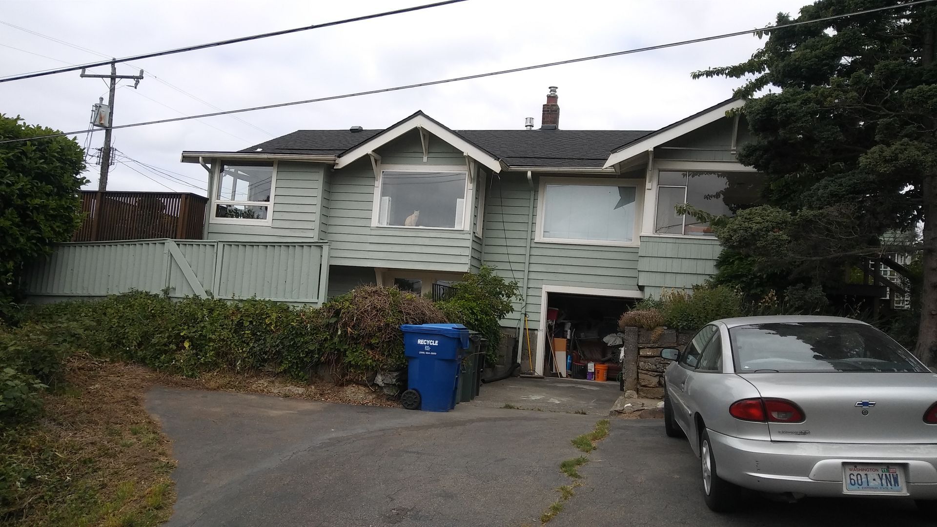 Suburban house with a silver car in the driveway, blue bin, and hedges along the front yard.