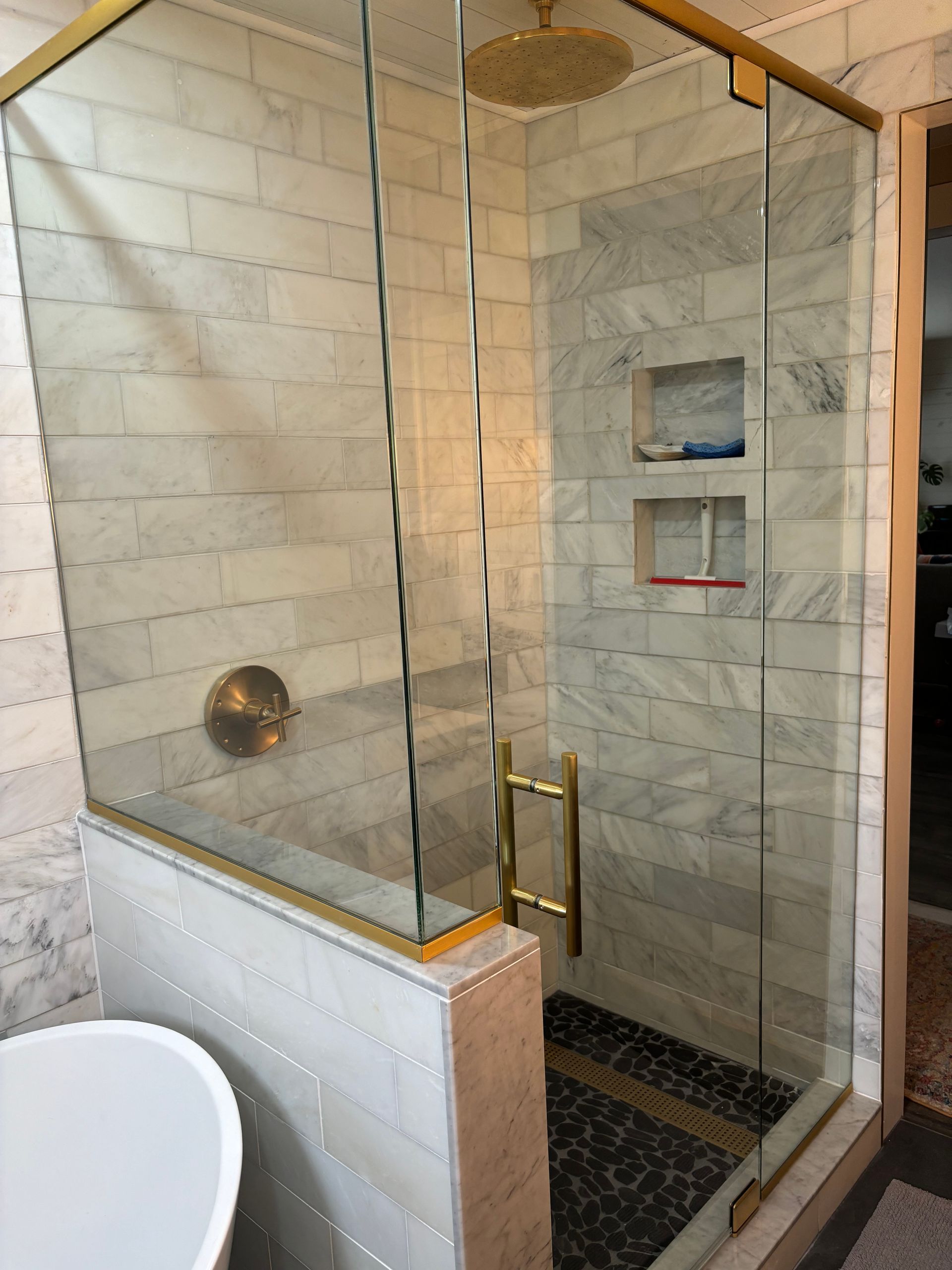 Glass shower enclosure with brass trim, tiled walls, and built-in shelves in a bathroom