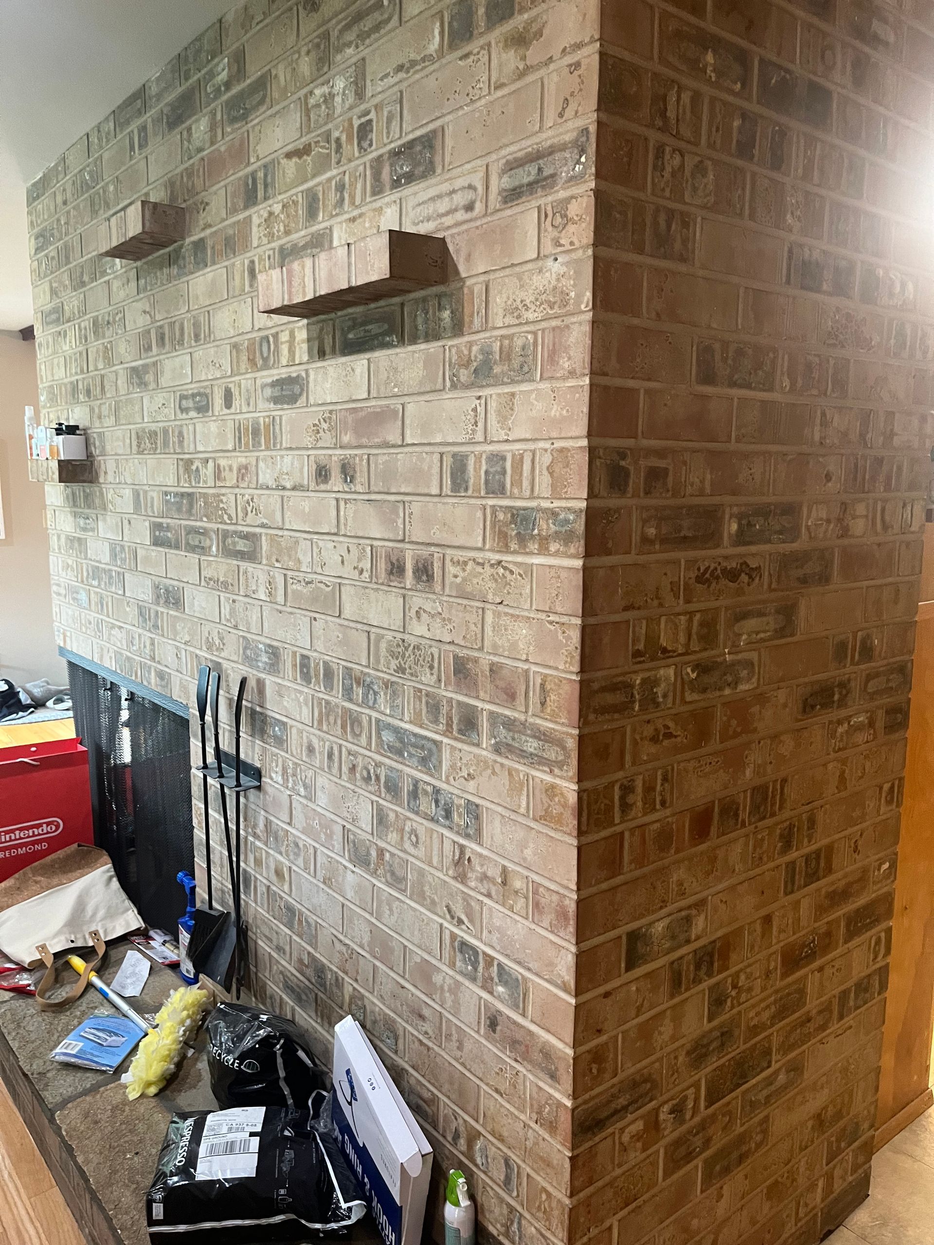Brick fireplace wall with recessed shelves and a cluttered hearth area in a living room
