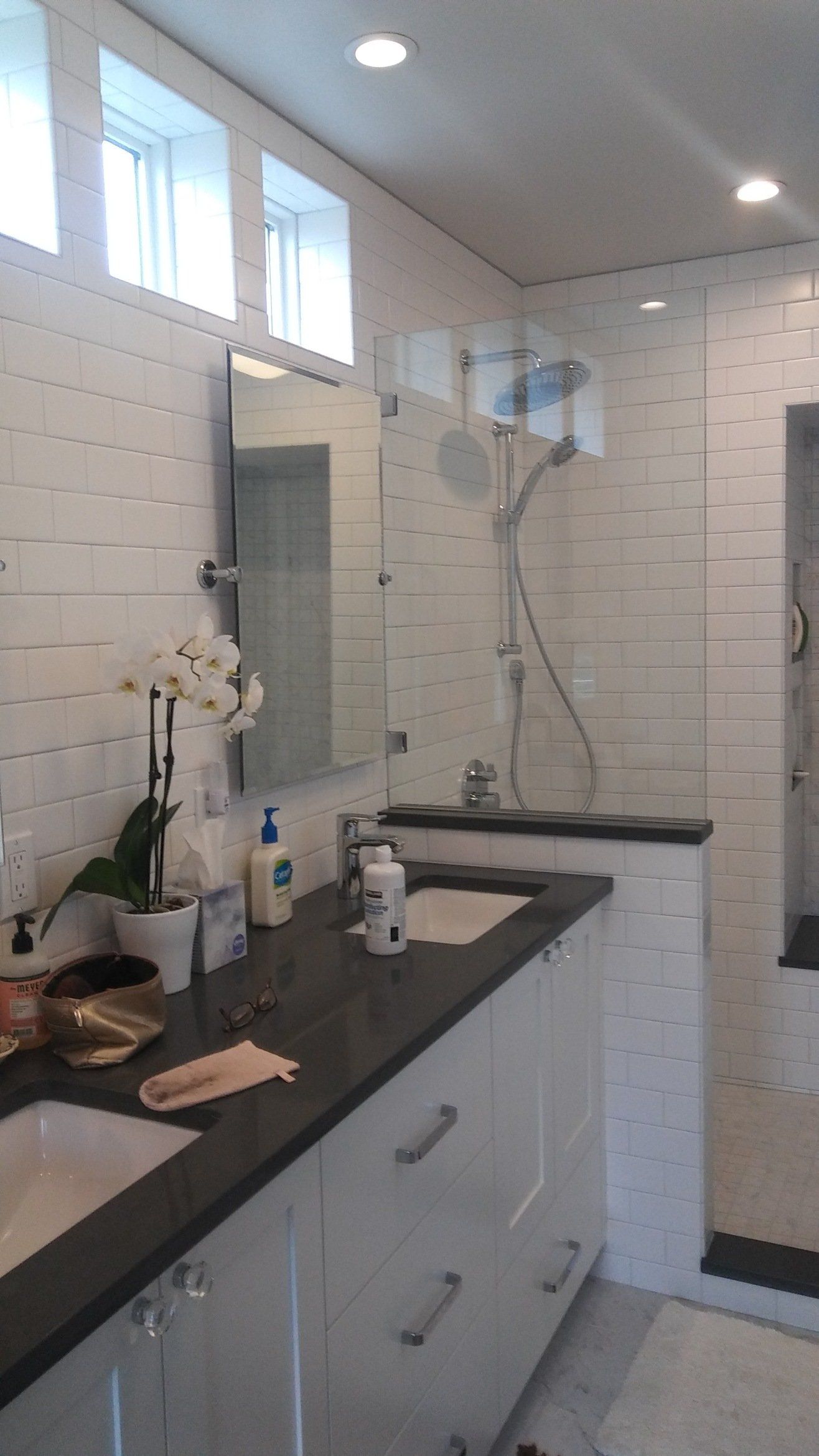 Modern bathroom with white tile, black vanity, mirror, and shower fixtures.