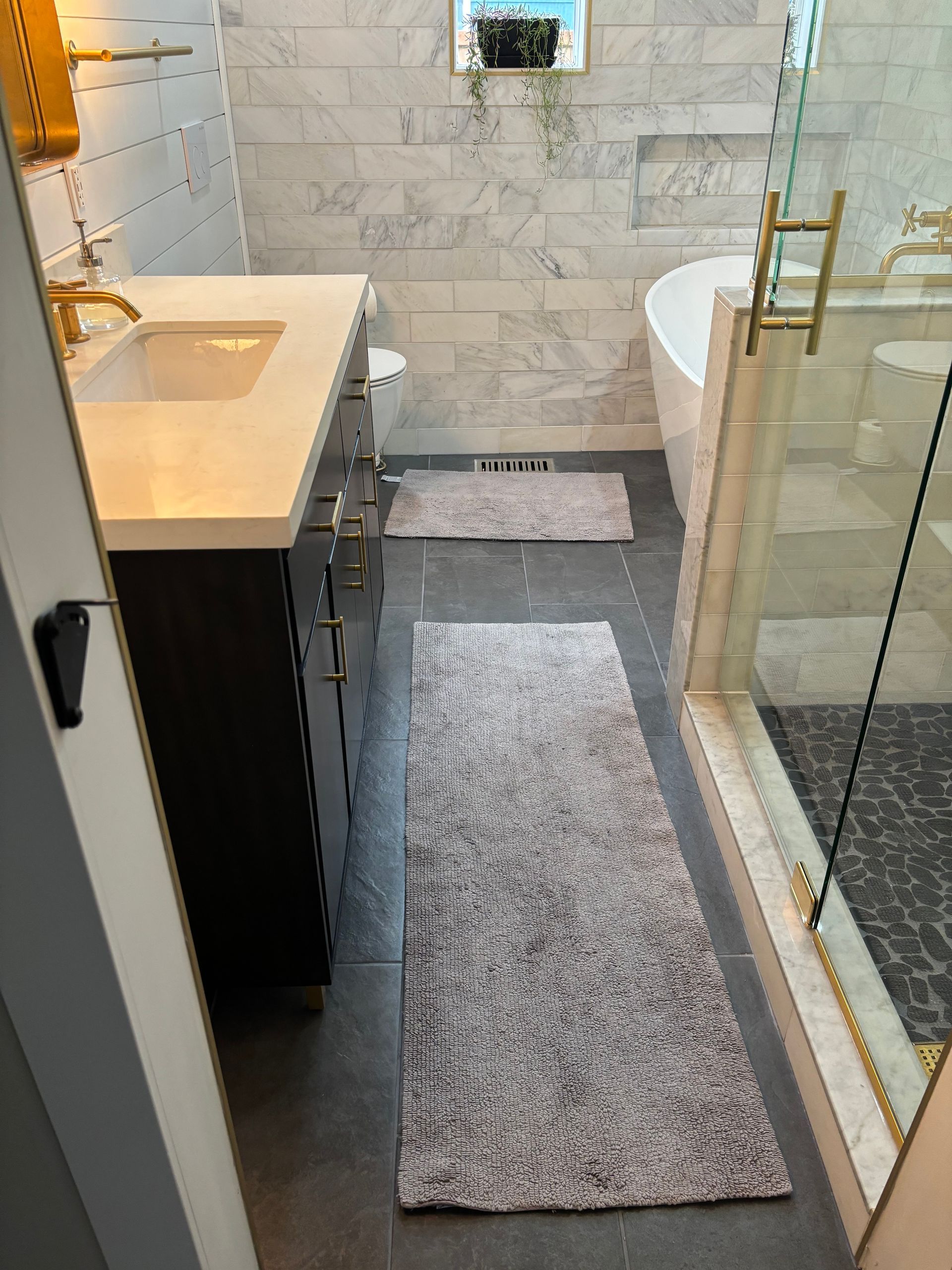 Narrow modern bathroom with a vanity, sink, toilet, glass shower, and gray runner rug.