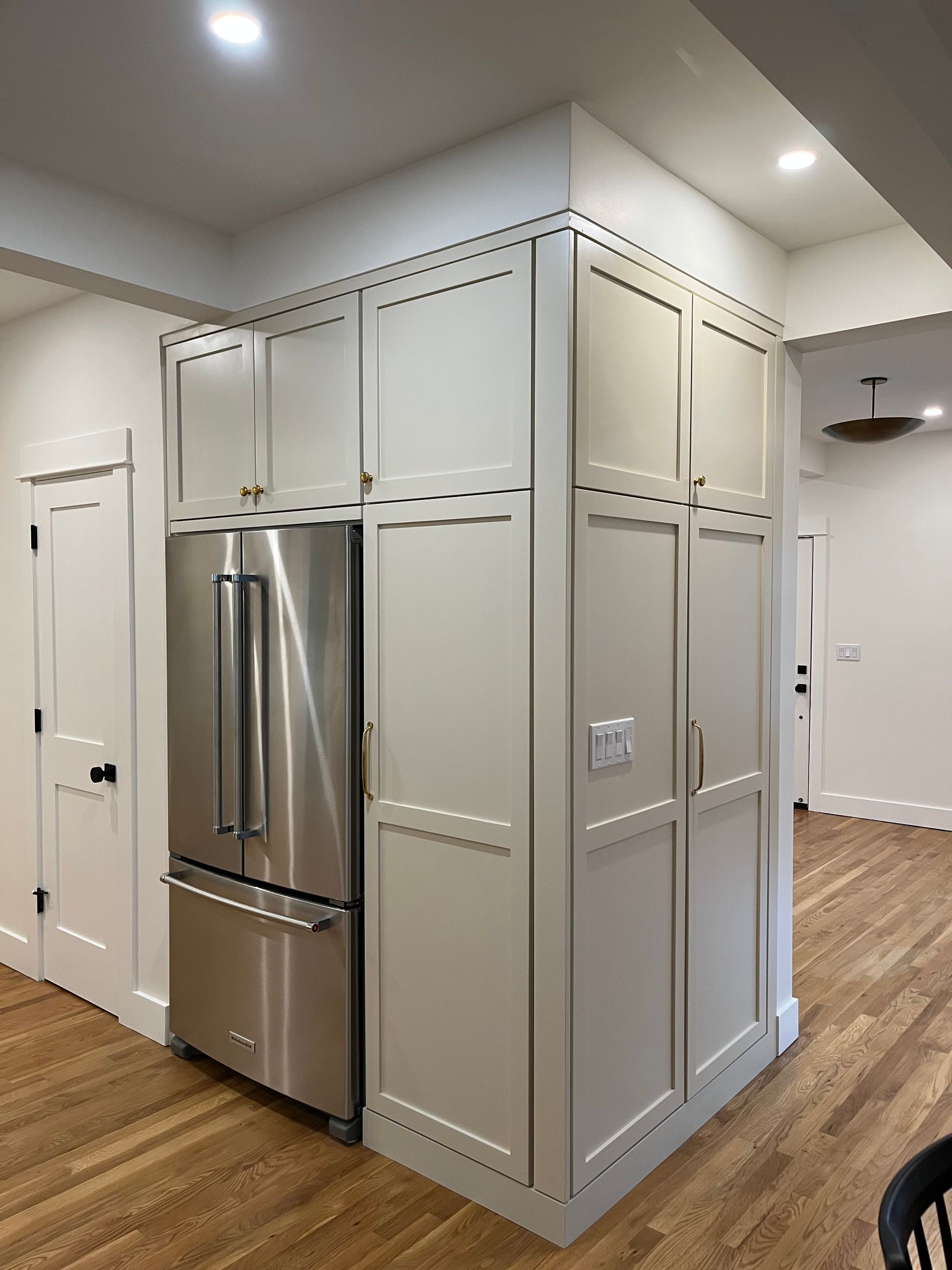 Kitchen with stainless steel refrigerator built into a white paneled cabinet wall and wood flooring