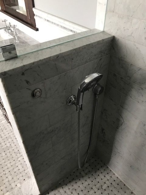Chrome handheld shower mounted on a marble shower wall with tiled floor below.
