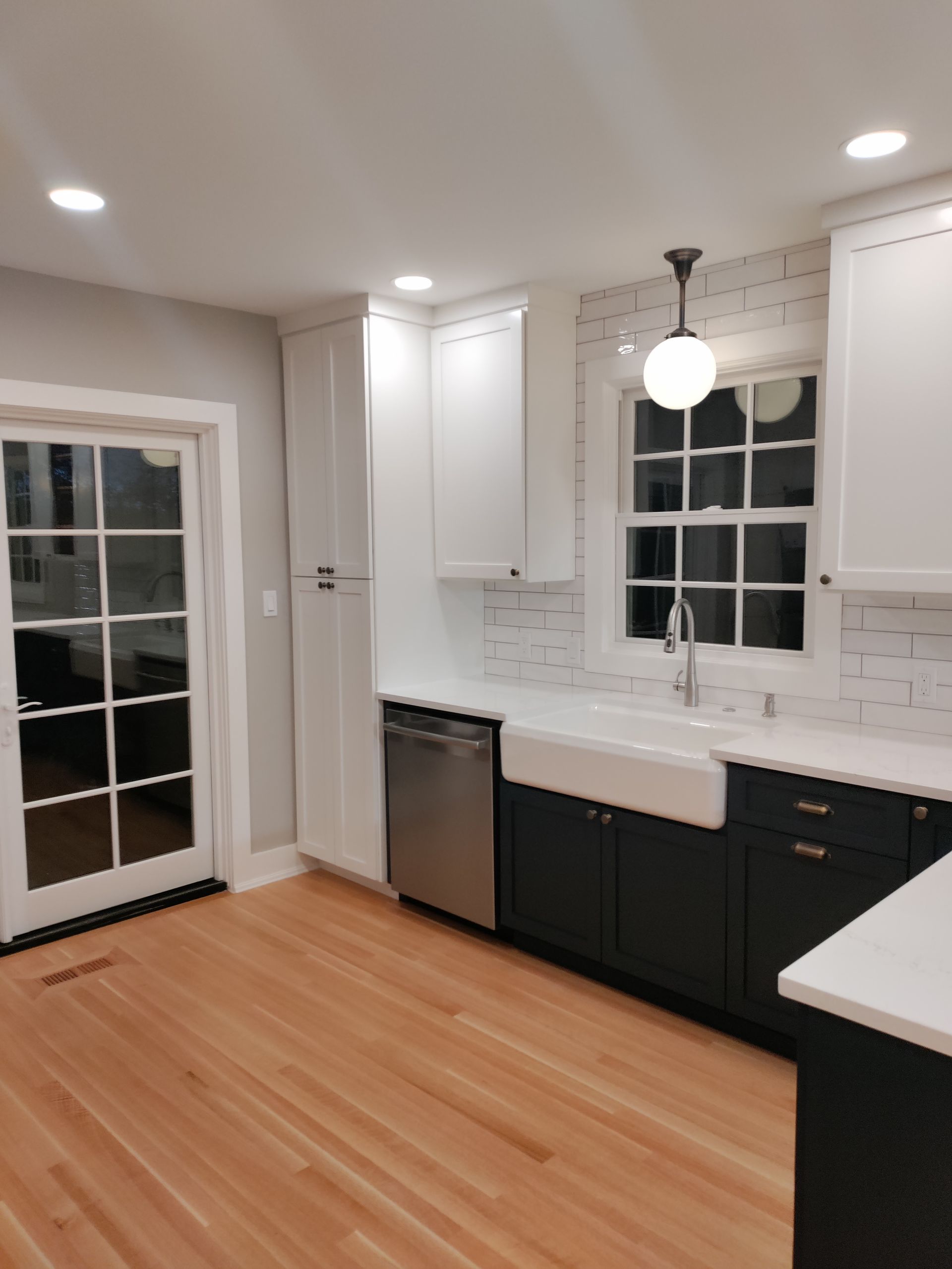 Bright modern kitchen with white cabinets, black lower cabinets, hardwood floors, and a glass door to a deck