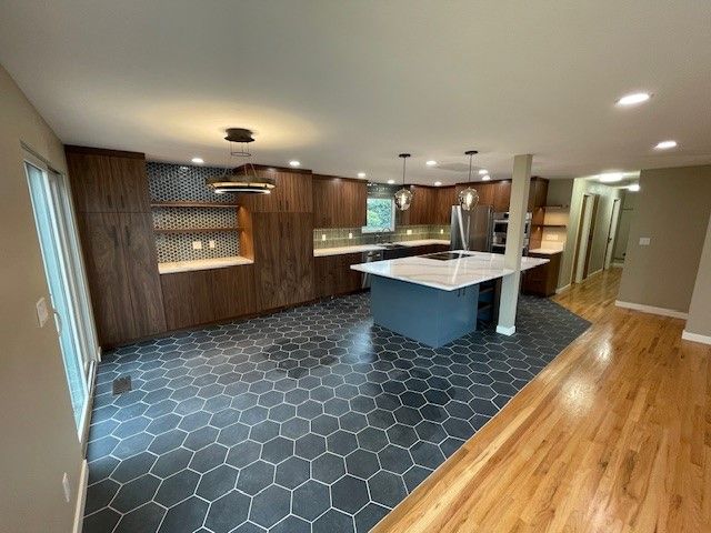 Modern open kitchen with dark wood cabinets, hex tile floor, white island, and hardwood dining area