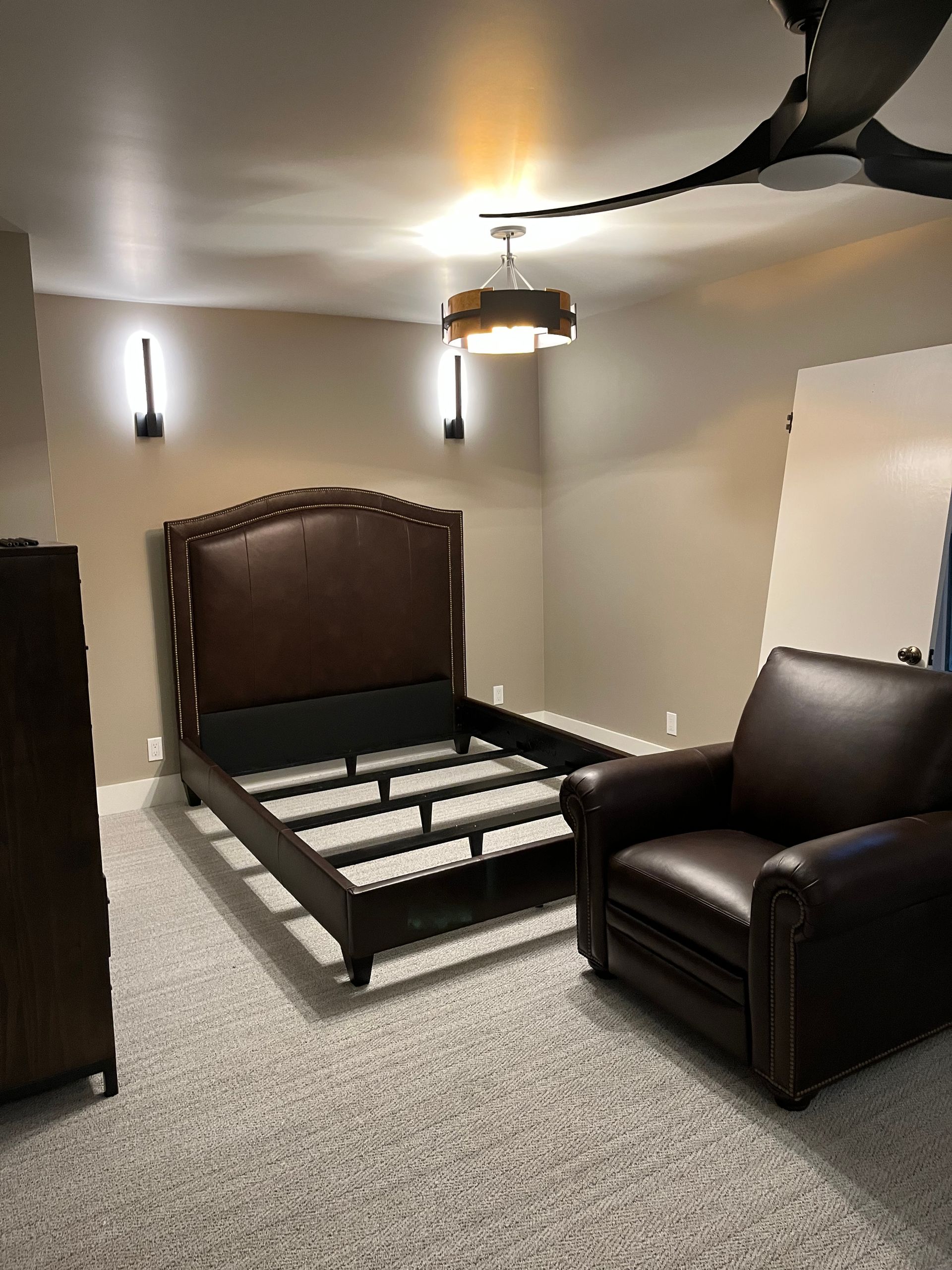 Bedroom with a bed frame, armchair, carpet, and ceiling fan in a neutral-toned room