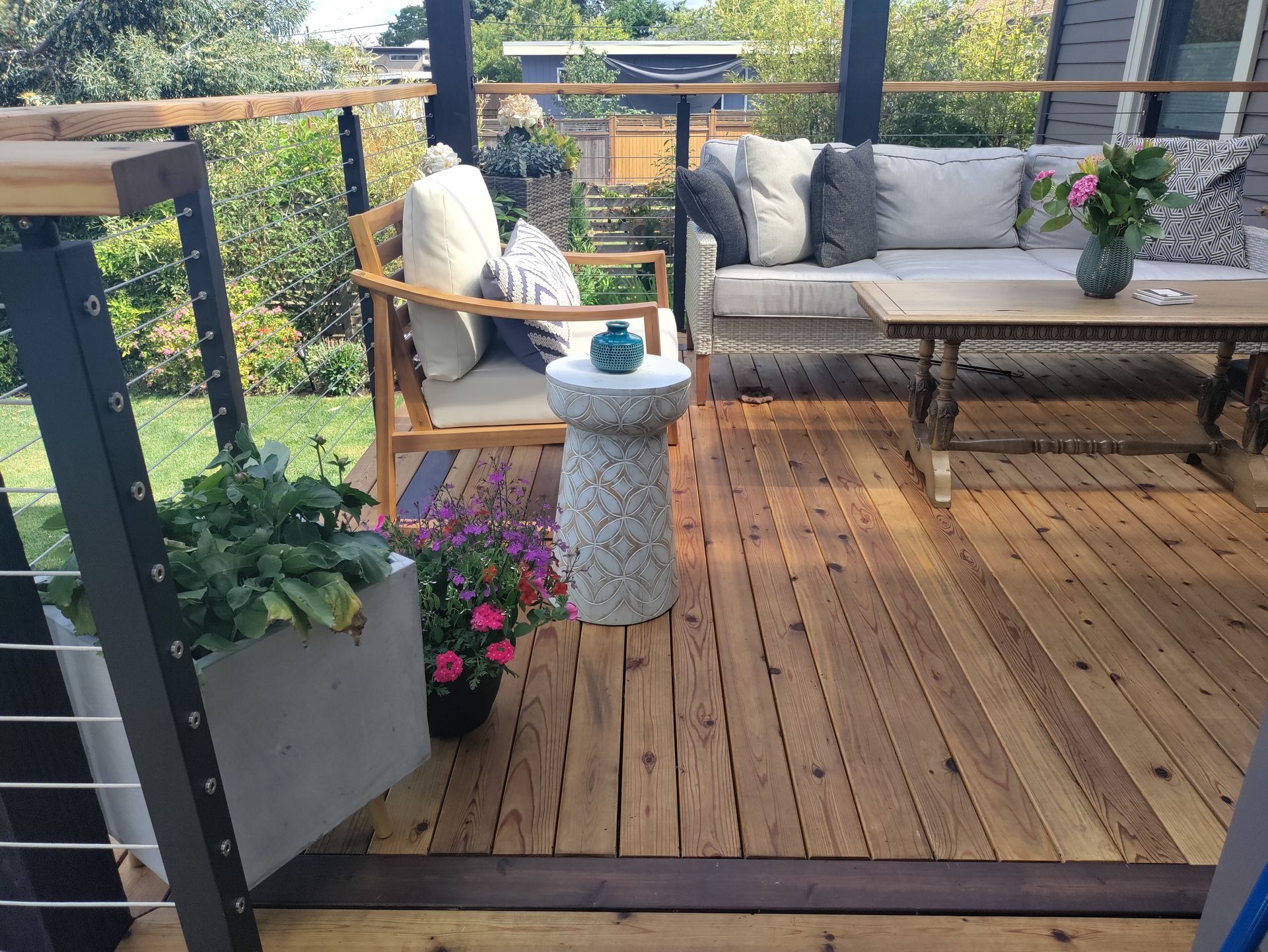 Wooden deck patio with outdoor seating, potted plants, and a small table under a covered area.