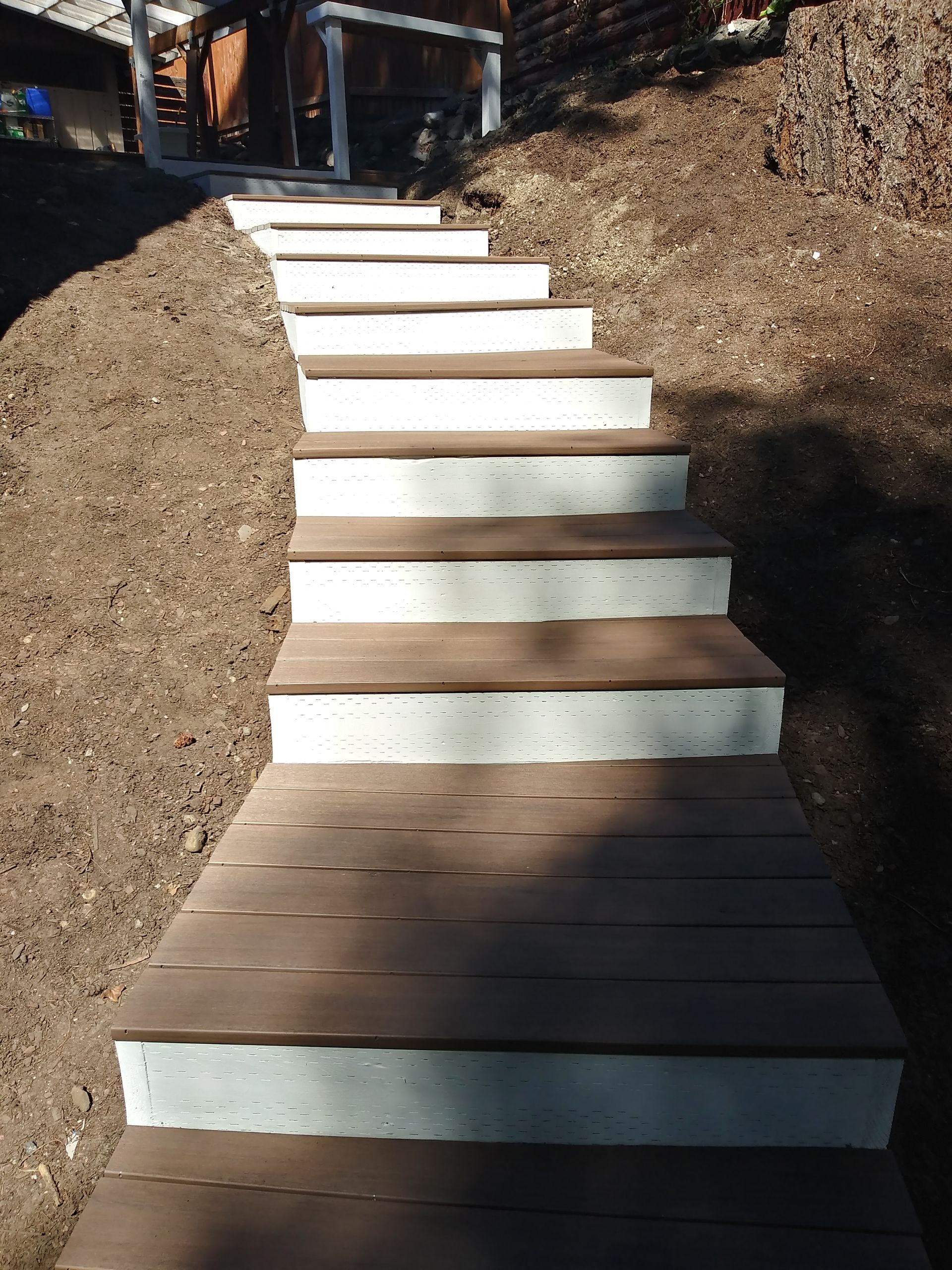 Outdoor concrete steps ascending a dirt slope, with white risers and brown treads