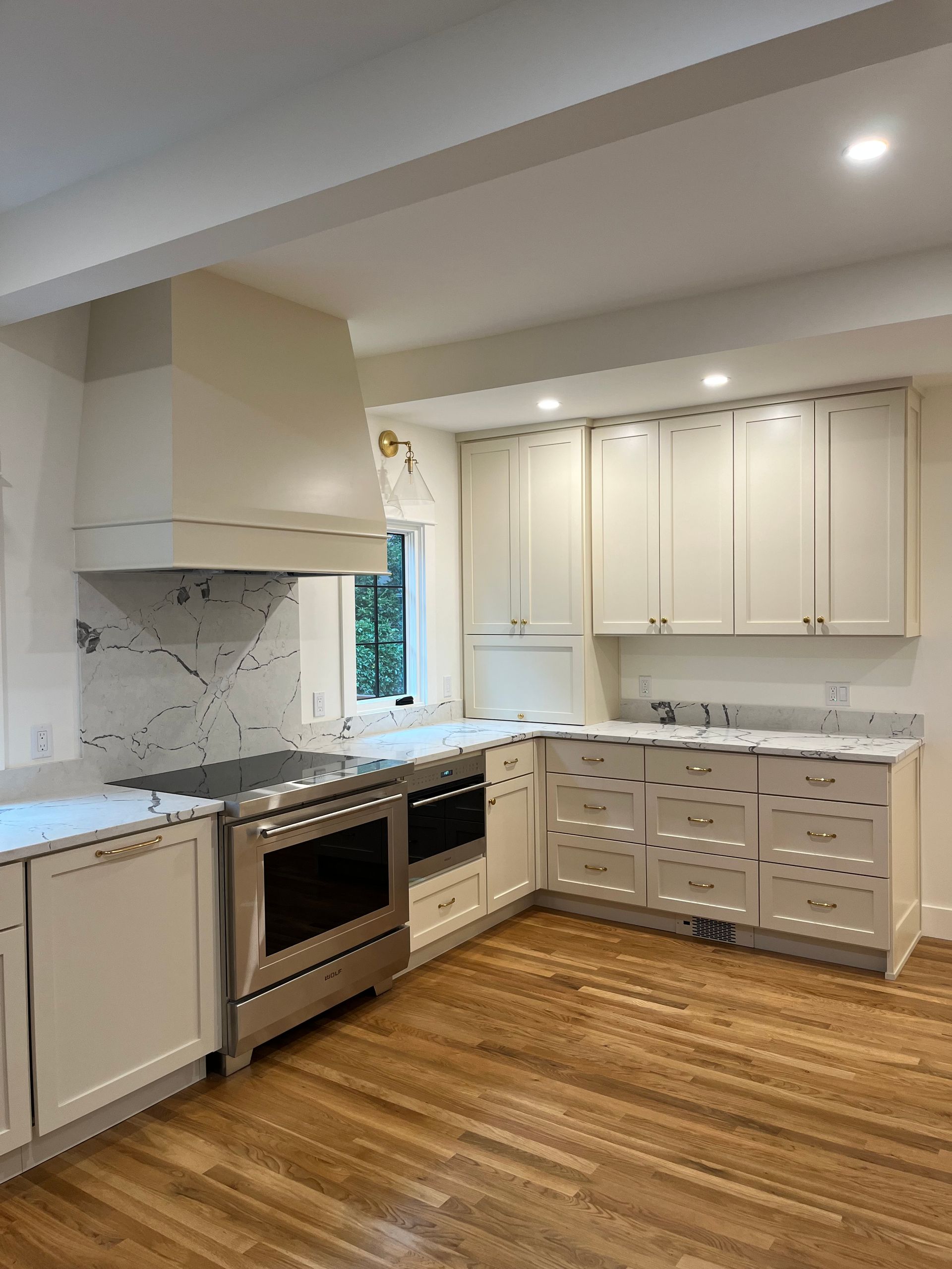 Bright white kitchen with wood floors, stainless oven, and white cabinets along an L-shaped counter.